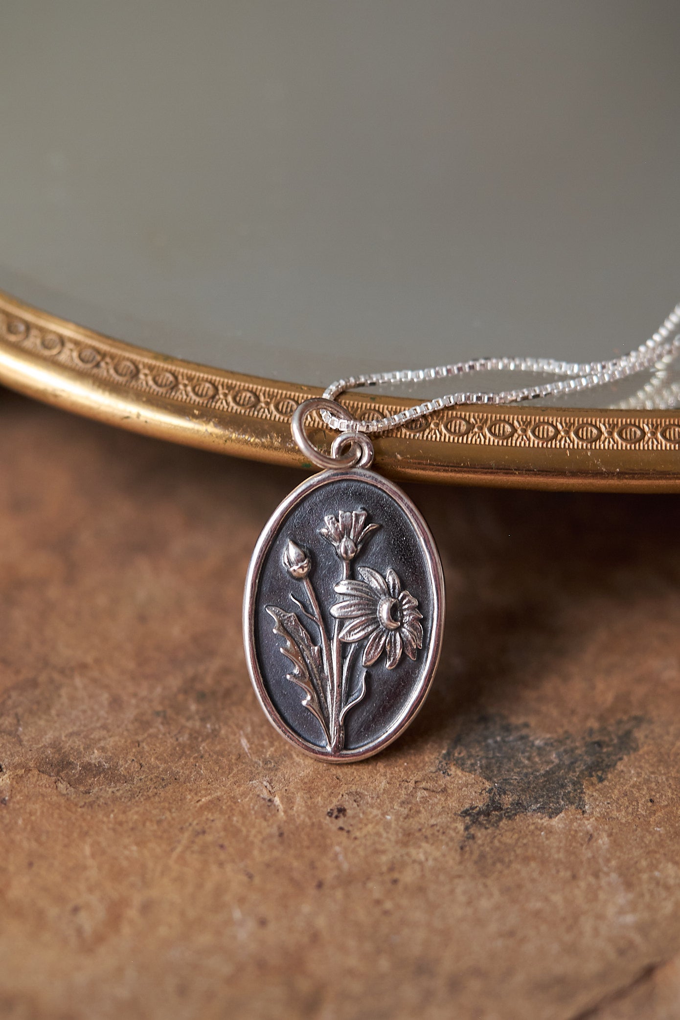 Silver pendant with floral design on a chain against a textured surface