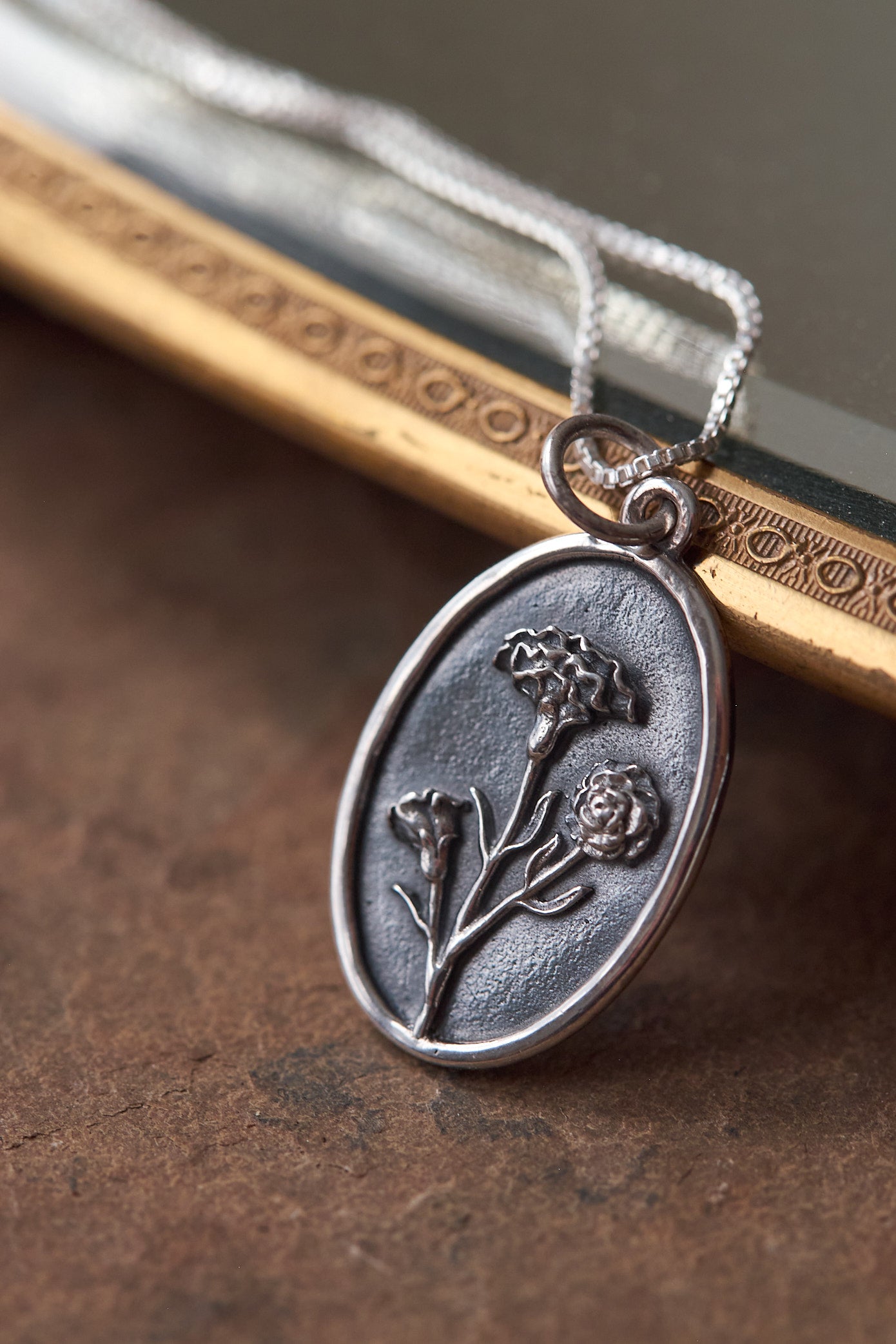 Silver carnation design pendant on a textured surface