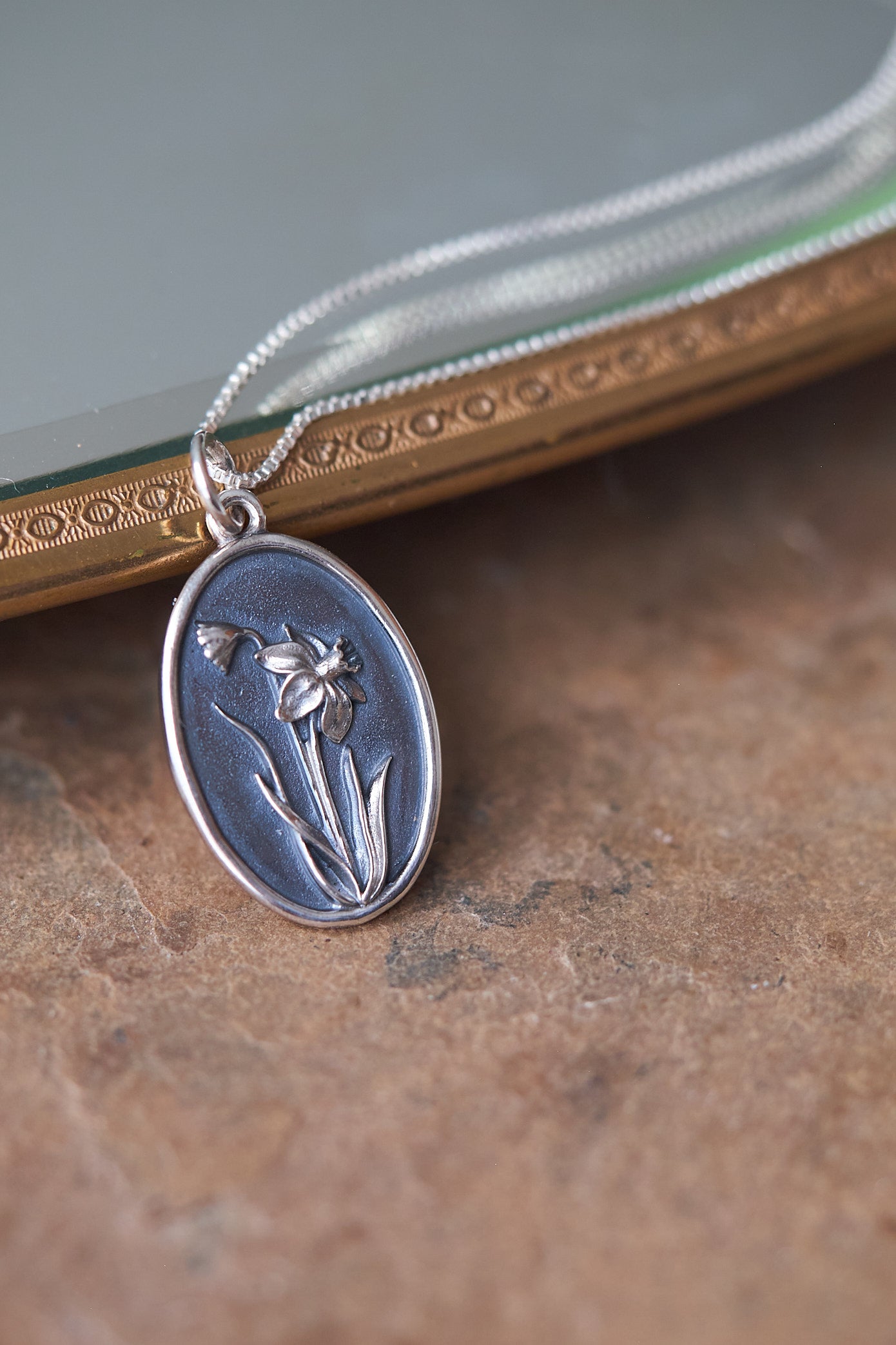 Silver pendant with daffodil flower design on a slate surface