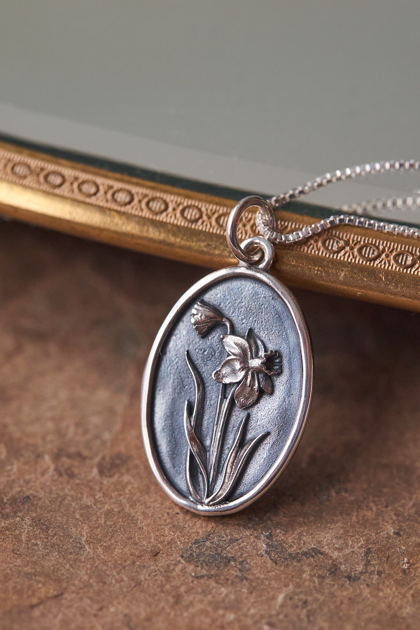 Silver pendant with daffodil flower design on a textured surface