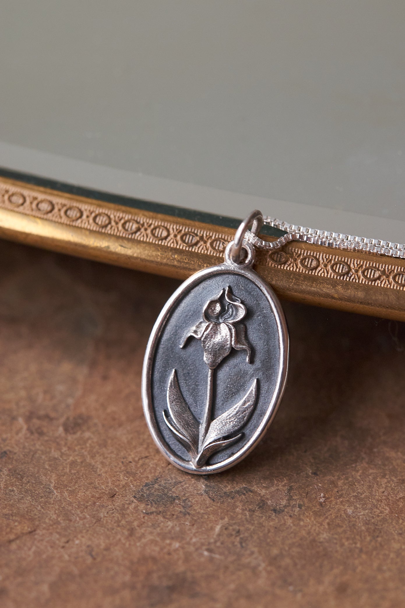 Silver pendant necklace with Iris flower design on a brown textured surface