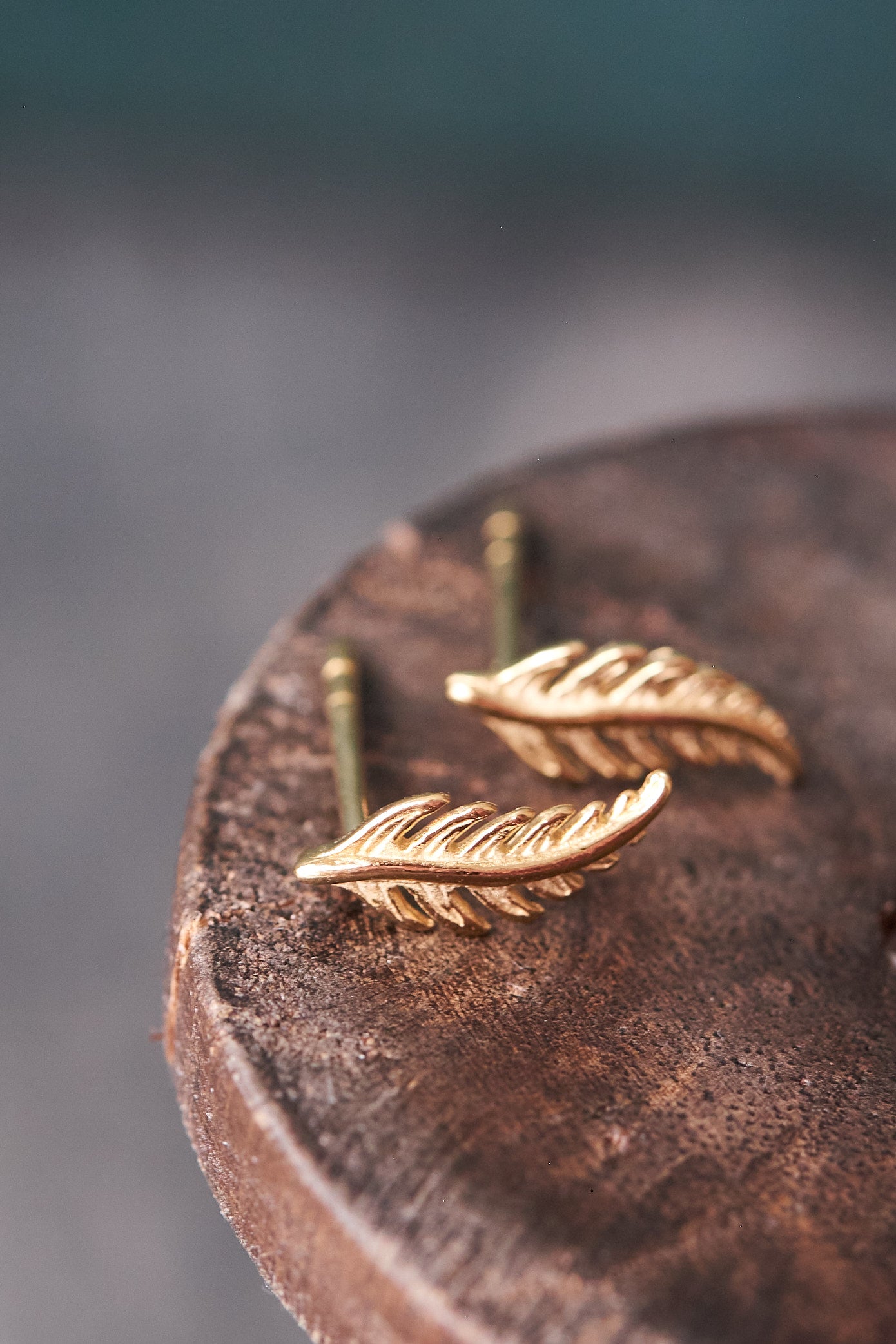 Gold fern-shaped earrings on a wooden surface with a blurred background