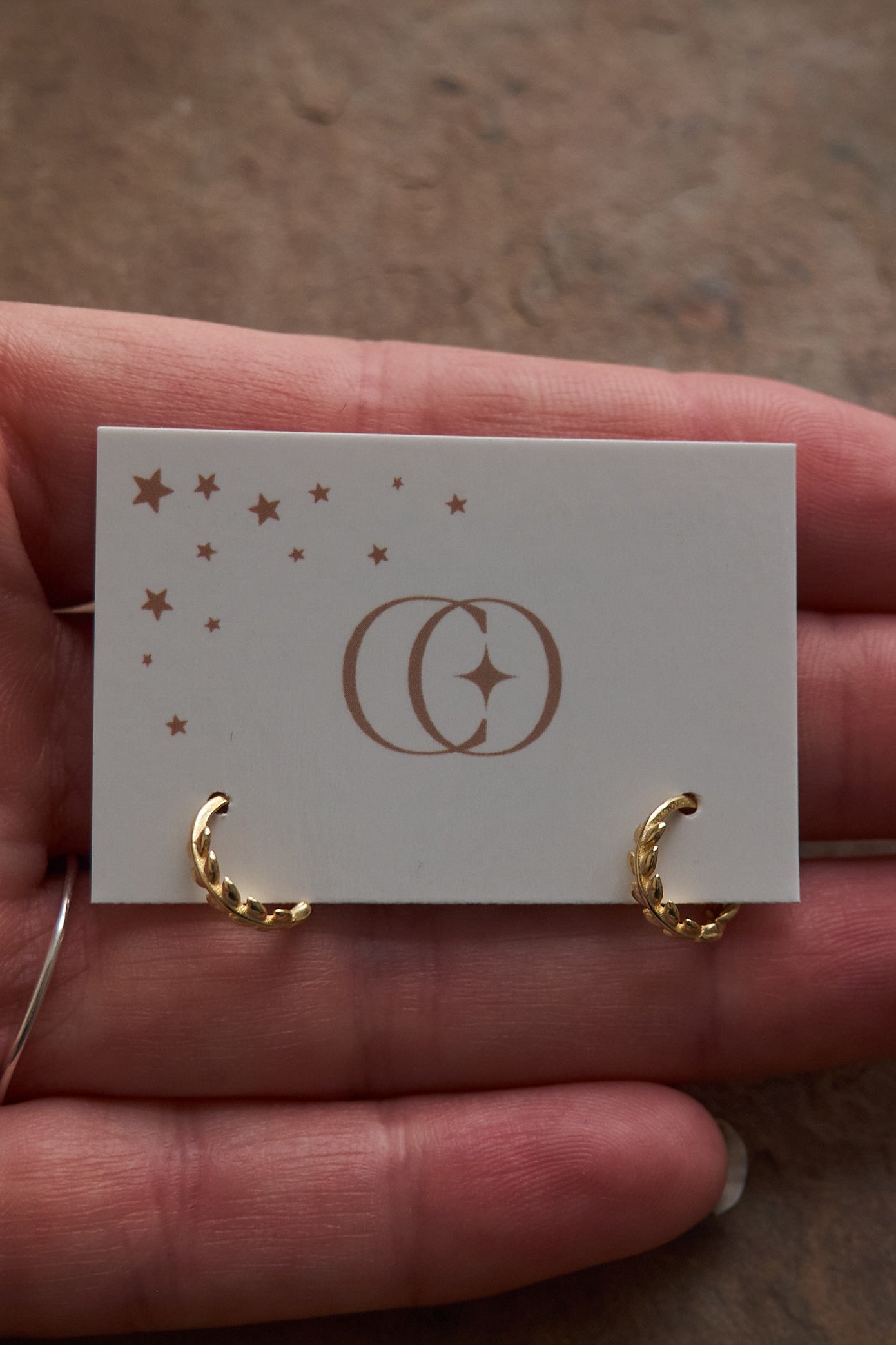 Gold hoop earrings on a card held in a hand with a blurred background