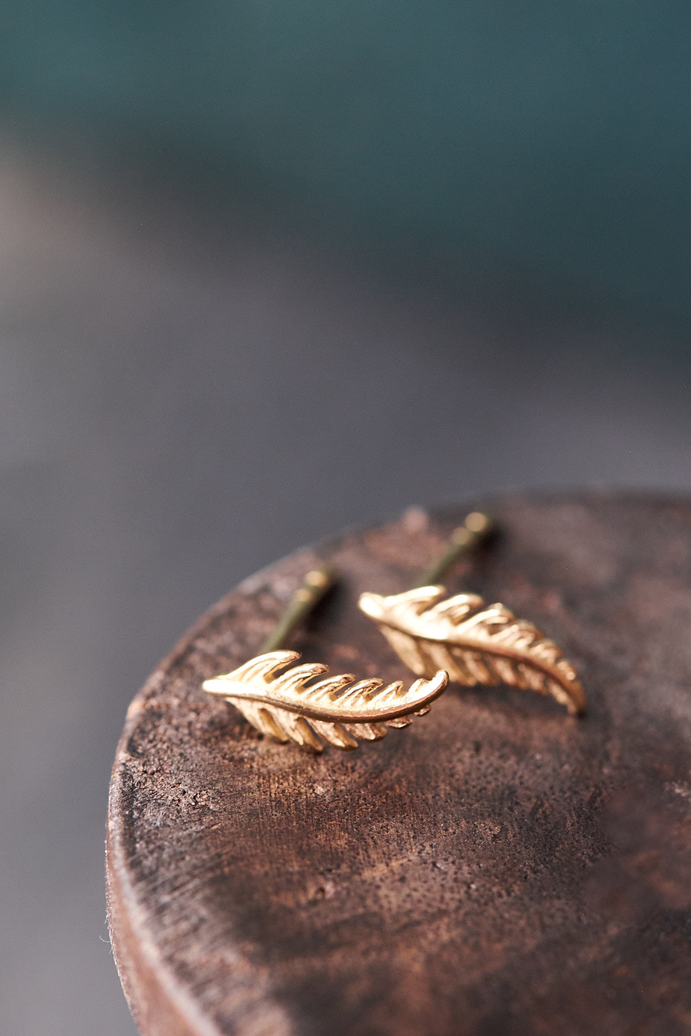 Gold feather-shaped earrings on a wooden surface with a blurred background