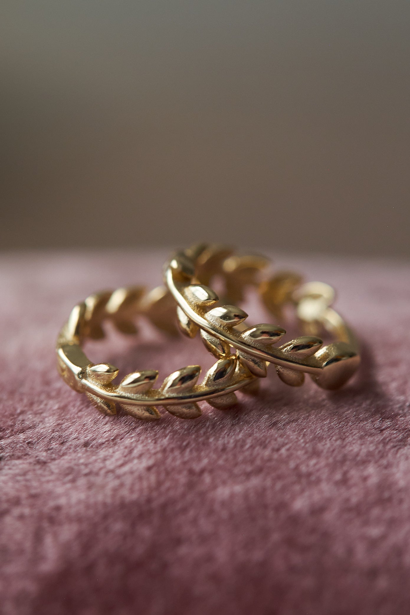 Pair of gold leaf hoop earrings on a soft pink surface