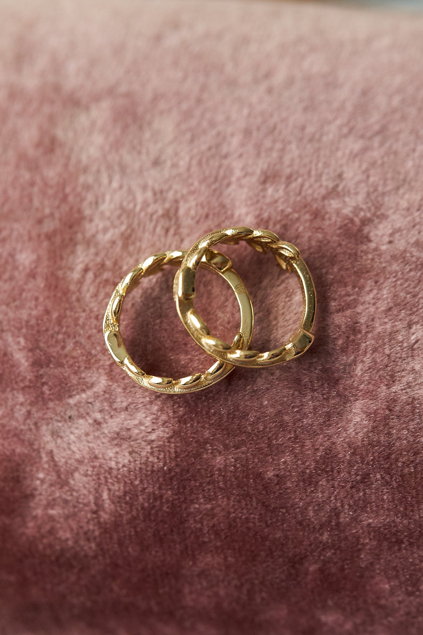 Two gold hoop earrings on a pink velvet surface