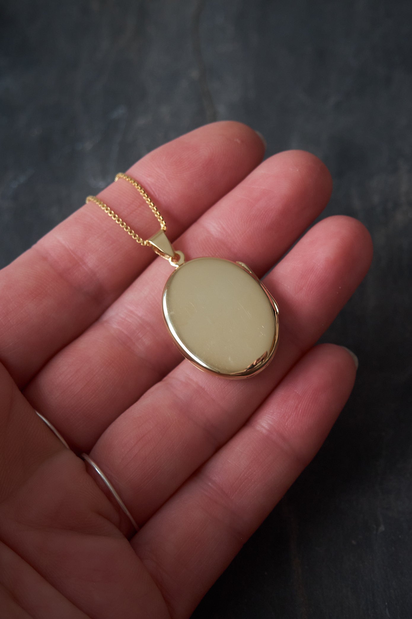 Gold locket necklace back shown in hand against a dark background