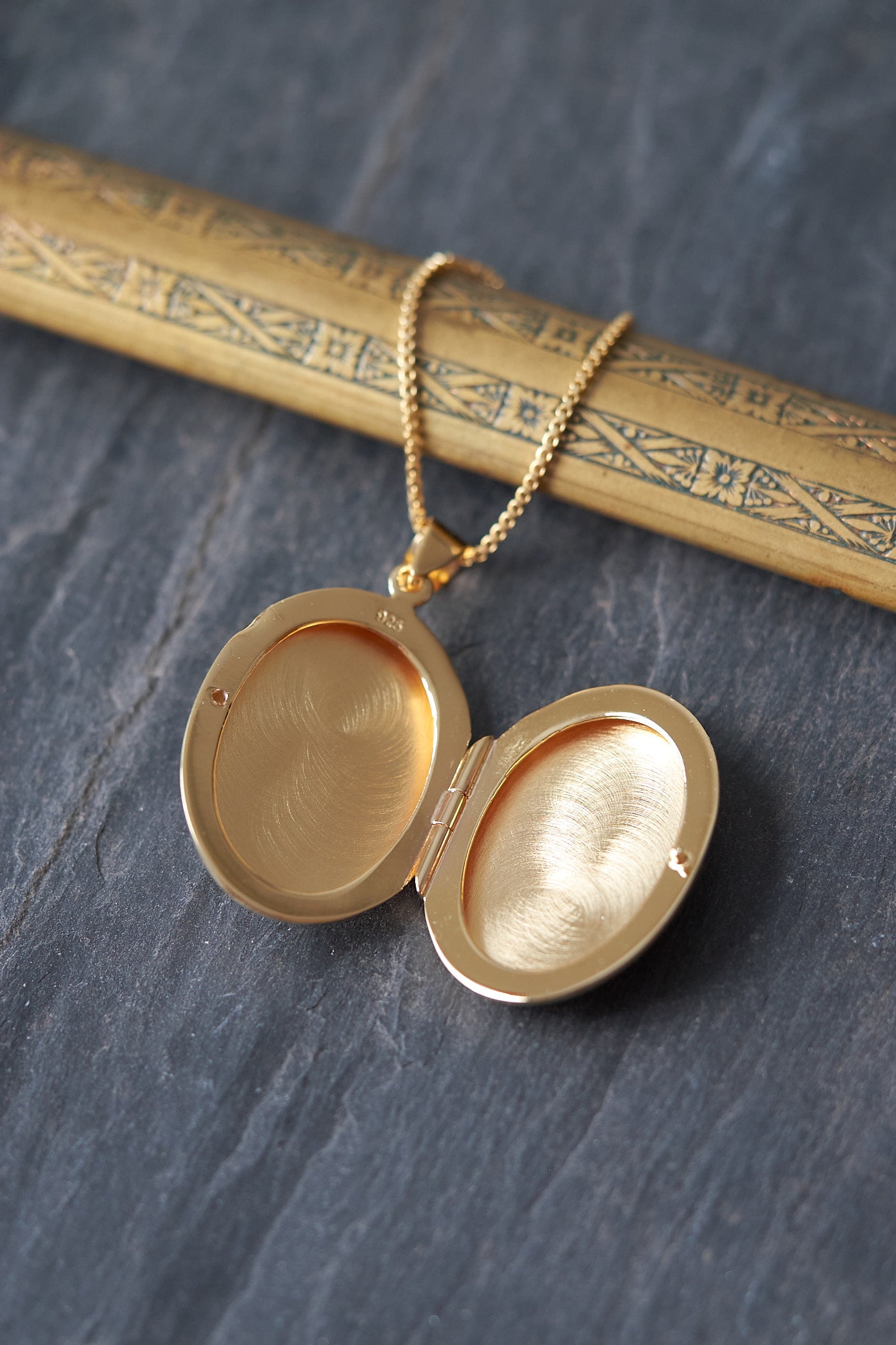 Gold locket with chain shown open on a textured dark surface