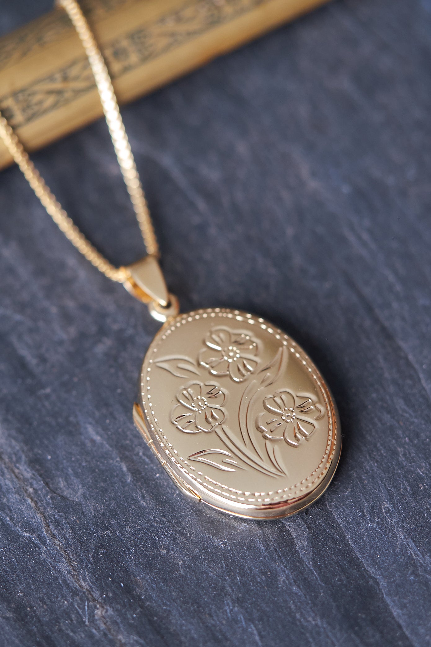 Gold oval locket with floral design on a dark slate surface