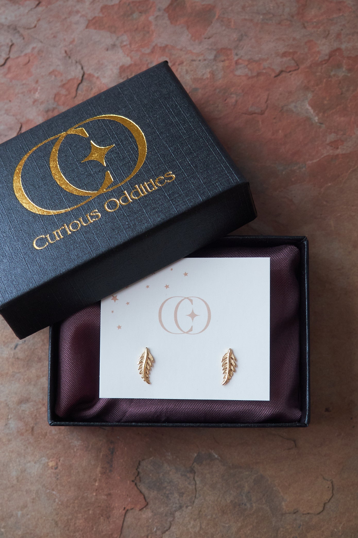 Gold leaf earrings in a 'Curious Oddities' box on a slate surface