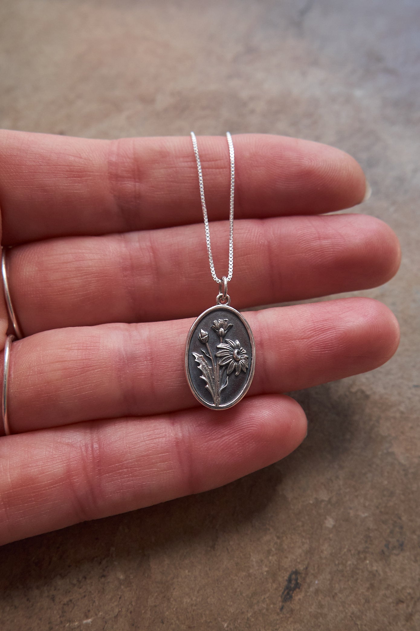 Silver necklace with a daisy pendant held in a hand on a neutral background