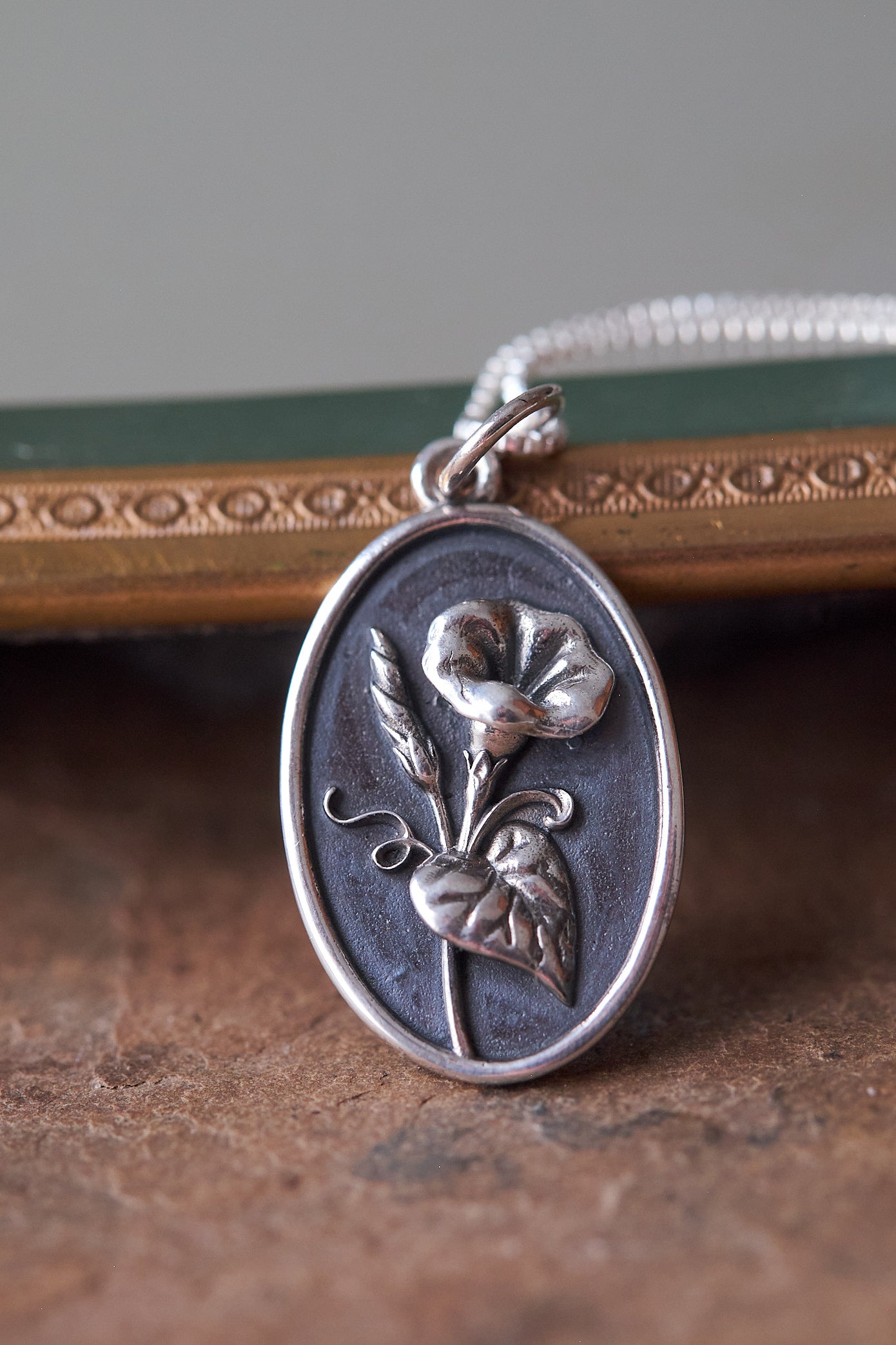 Silver pendant with Morning Glory design on a textured slate surface