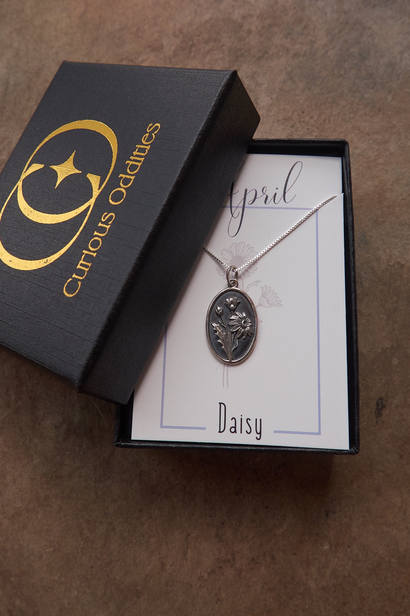 Silver necklace with floral pendant in a 'Curious Oddities' box on a brown surface
