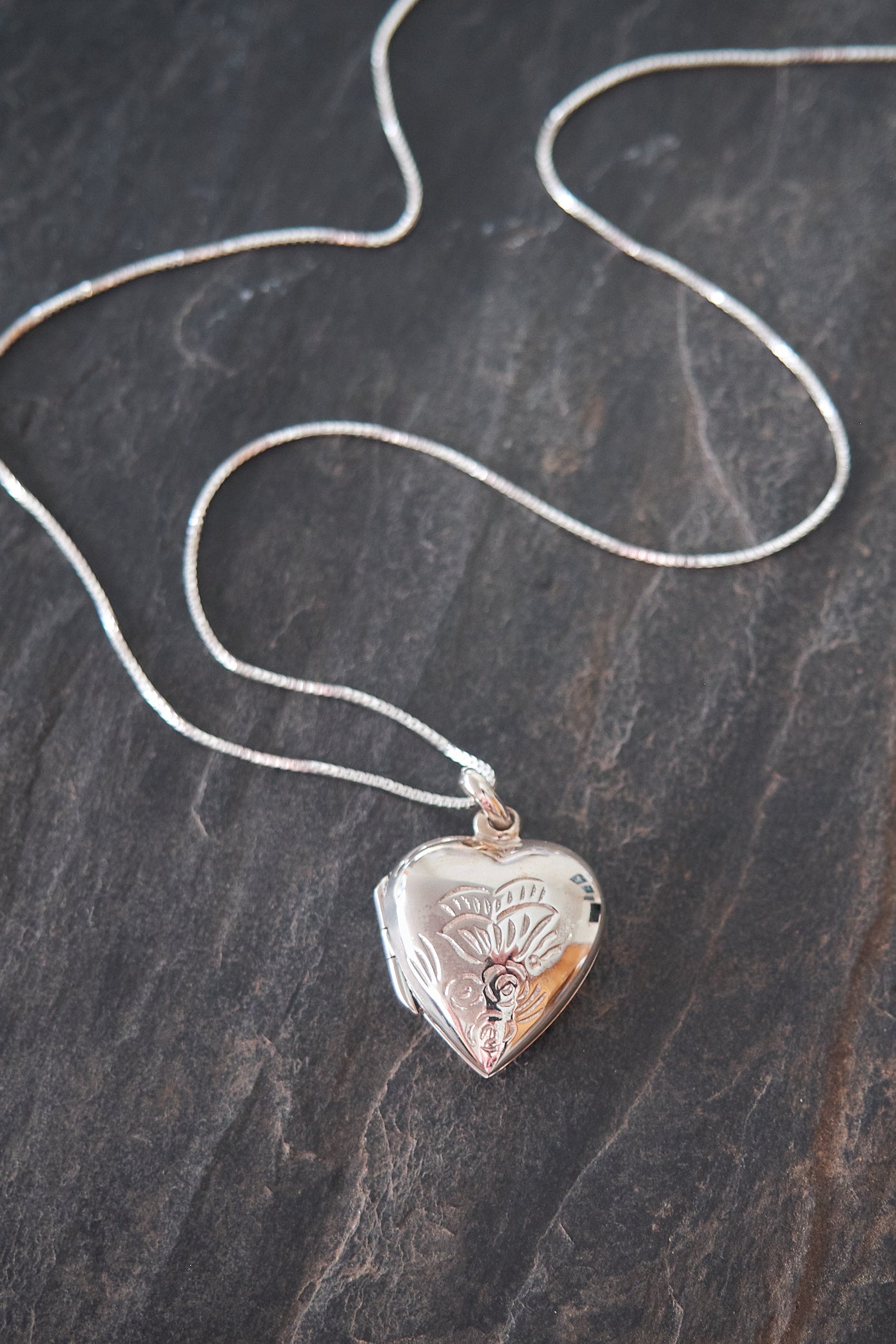 Heart-shaped locket on a chain against a dark stone background