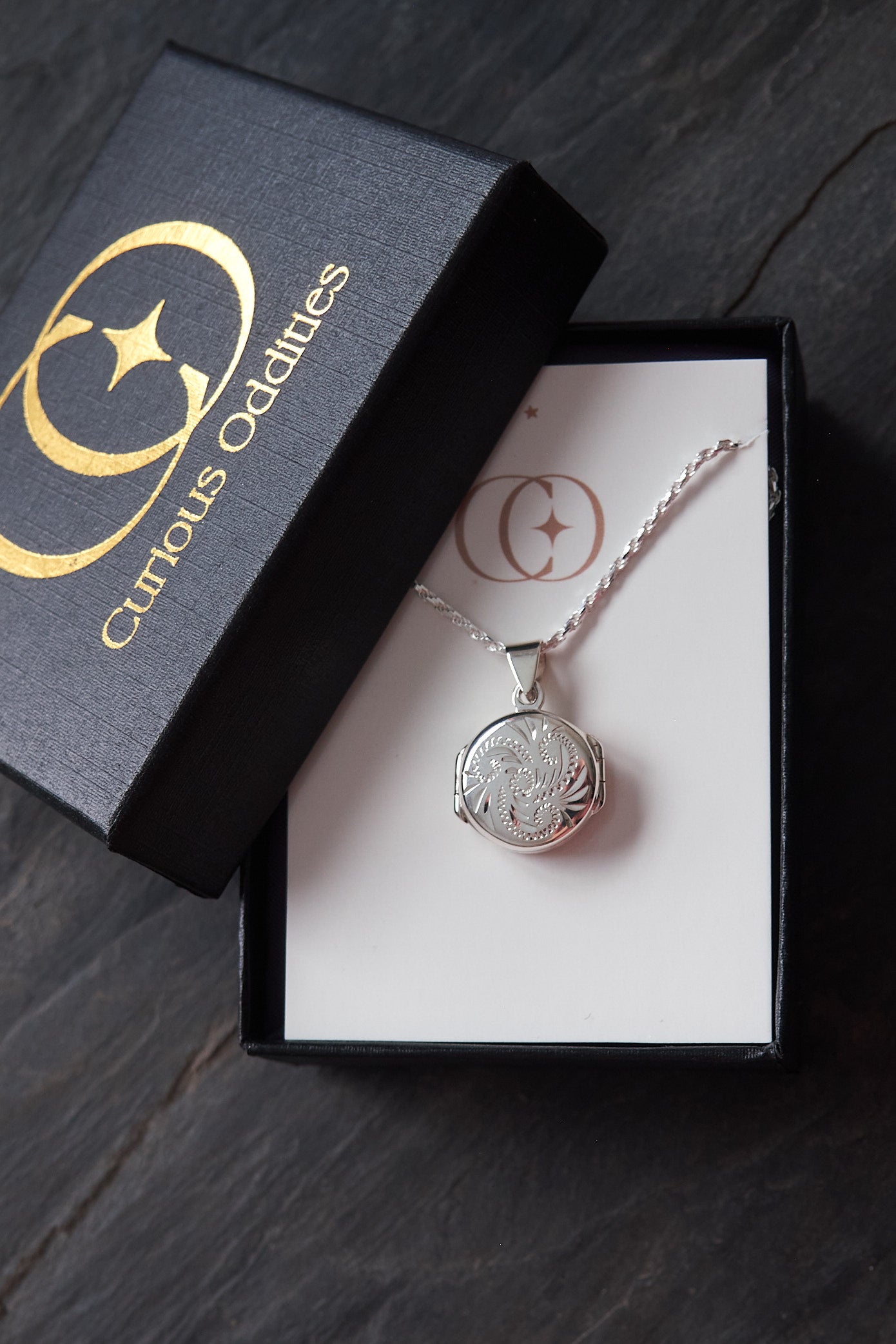 Silver necklace with a round locket pendant in a 'Curious Oddities' box on a dark surface