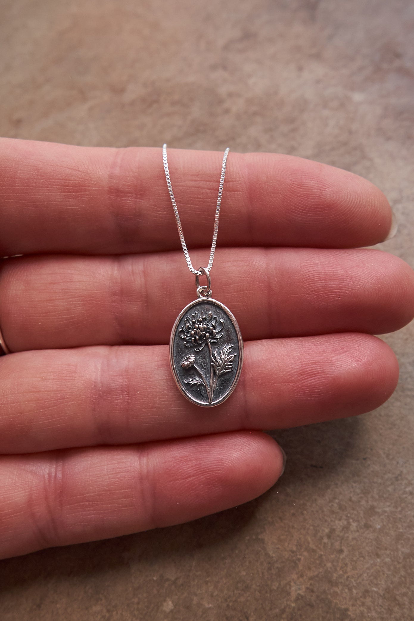 Silver necklace with a floral pendant held in hand on a brown slate surface