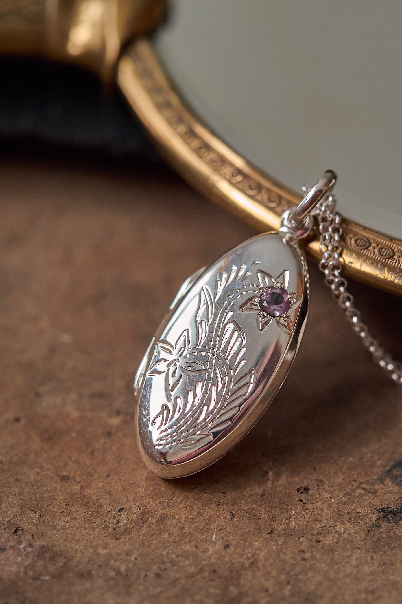 Silver oval locket with intricate designs on a textured surface