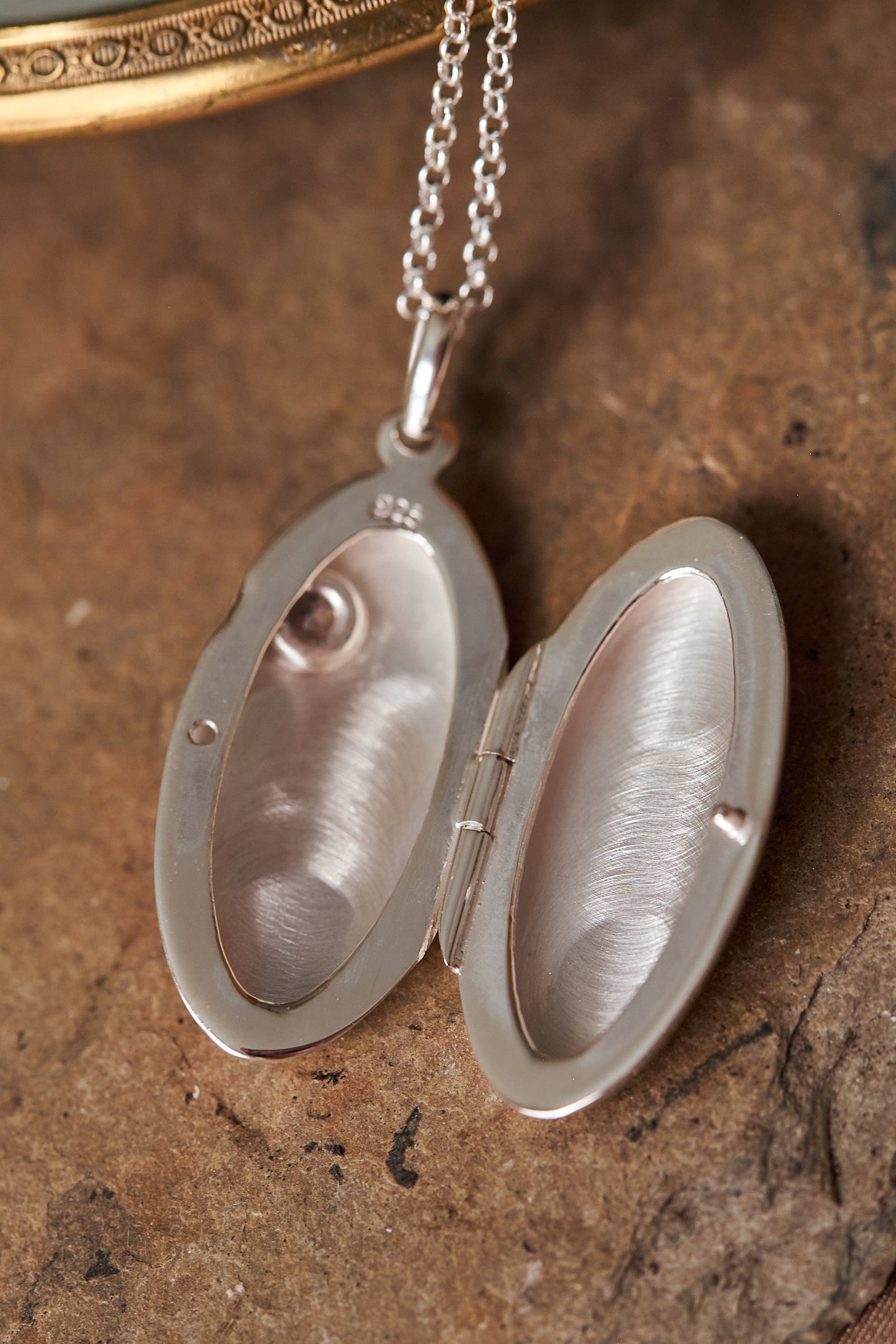 Silver oval locket on a chain pictured open against a textured brown background
