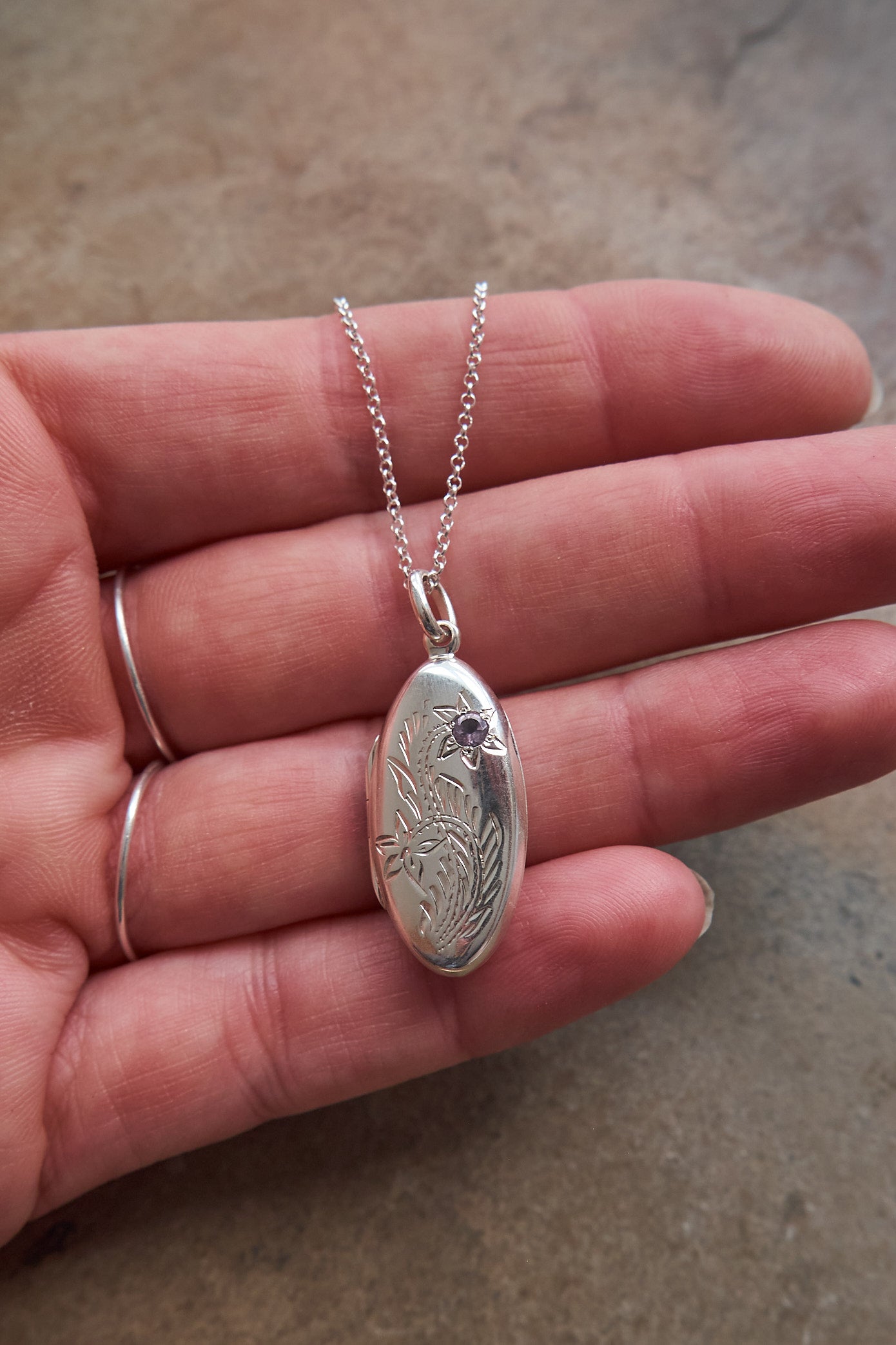 Silver locket pendant necklace held in a hand on a neutral background
