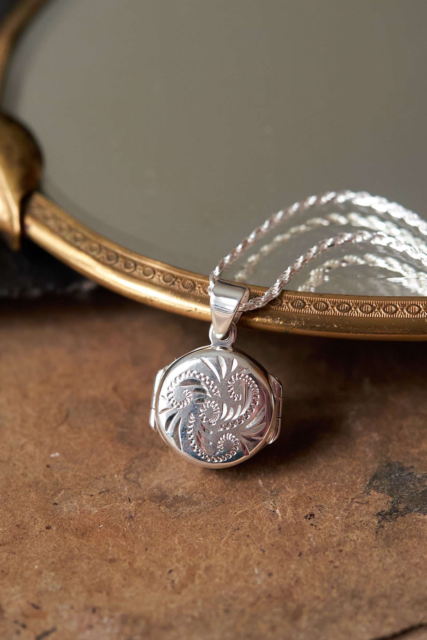 Silver pendant on a chain with intricate design, placed on a textured surface.