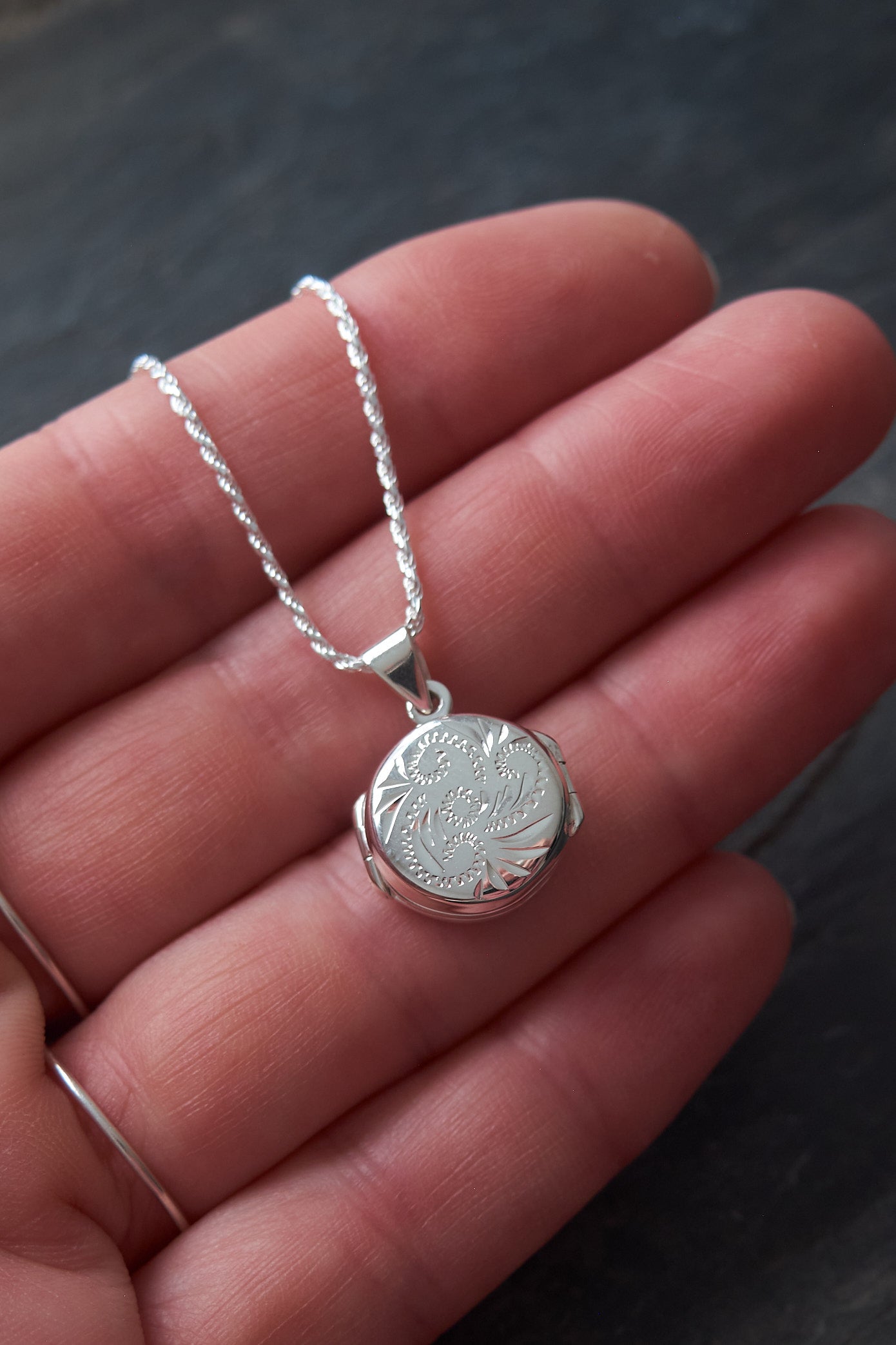 Silver necklace with a round locket pendant held in a hand against a dark background