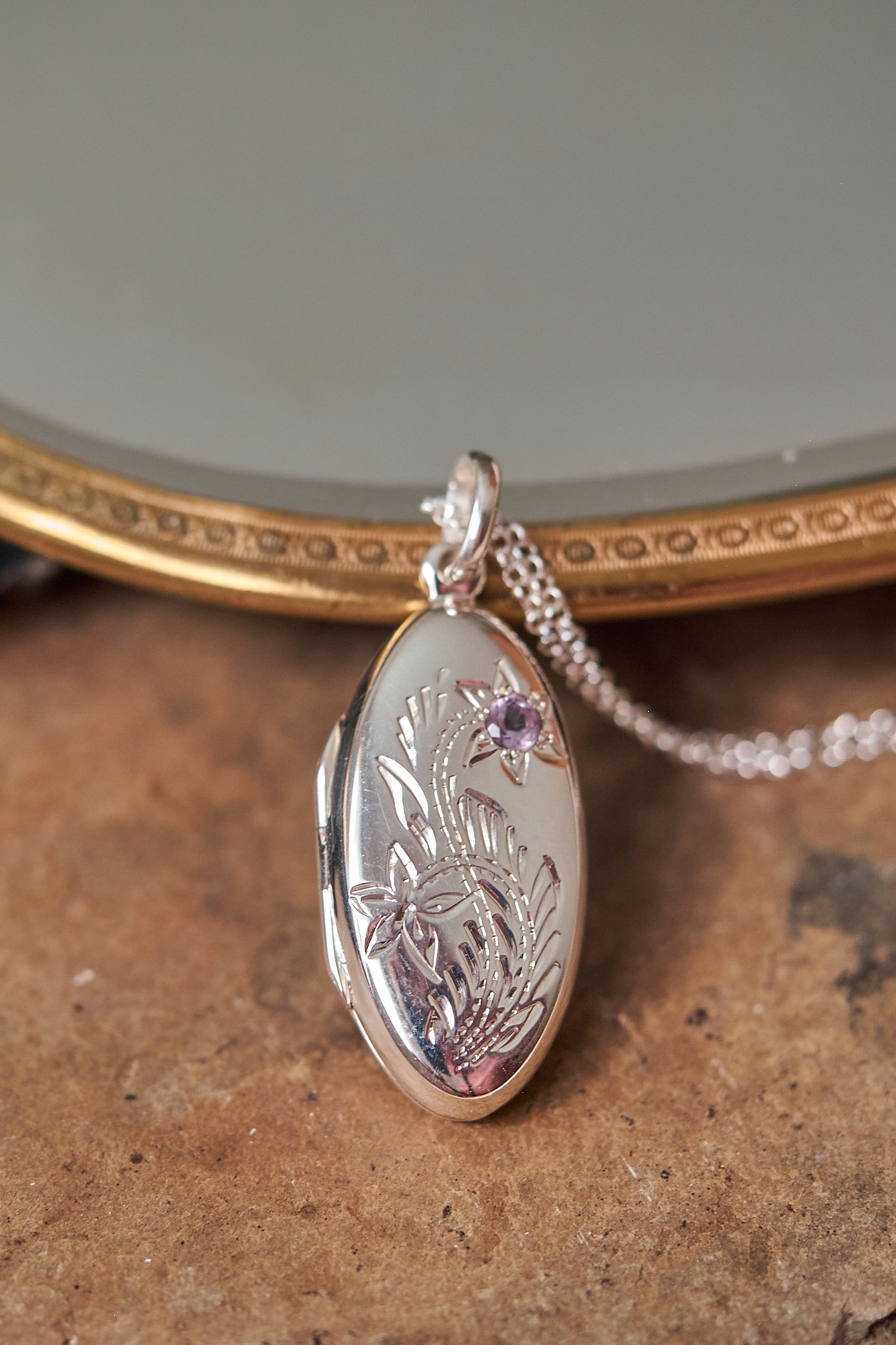 Silver locket with floral engraving on a textured surface