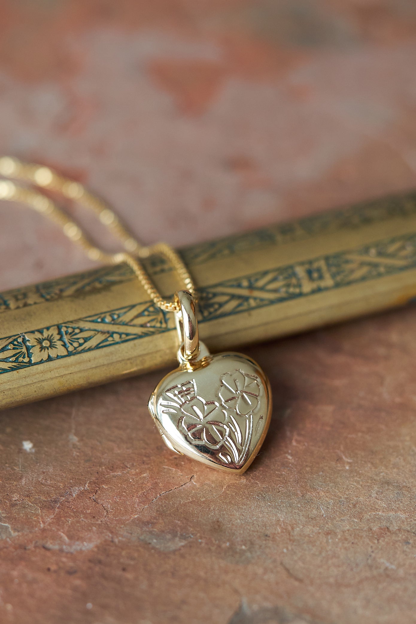Gold heart-shaped locket pendant on a chain with a textured surface background