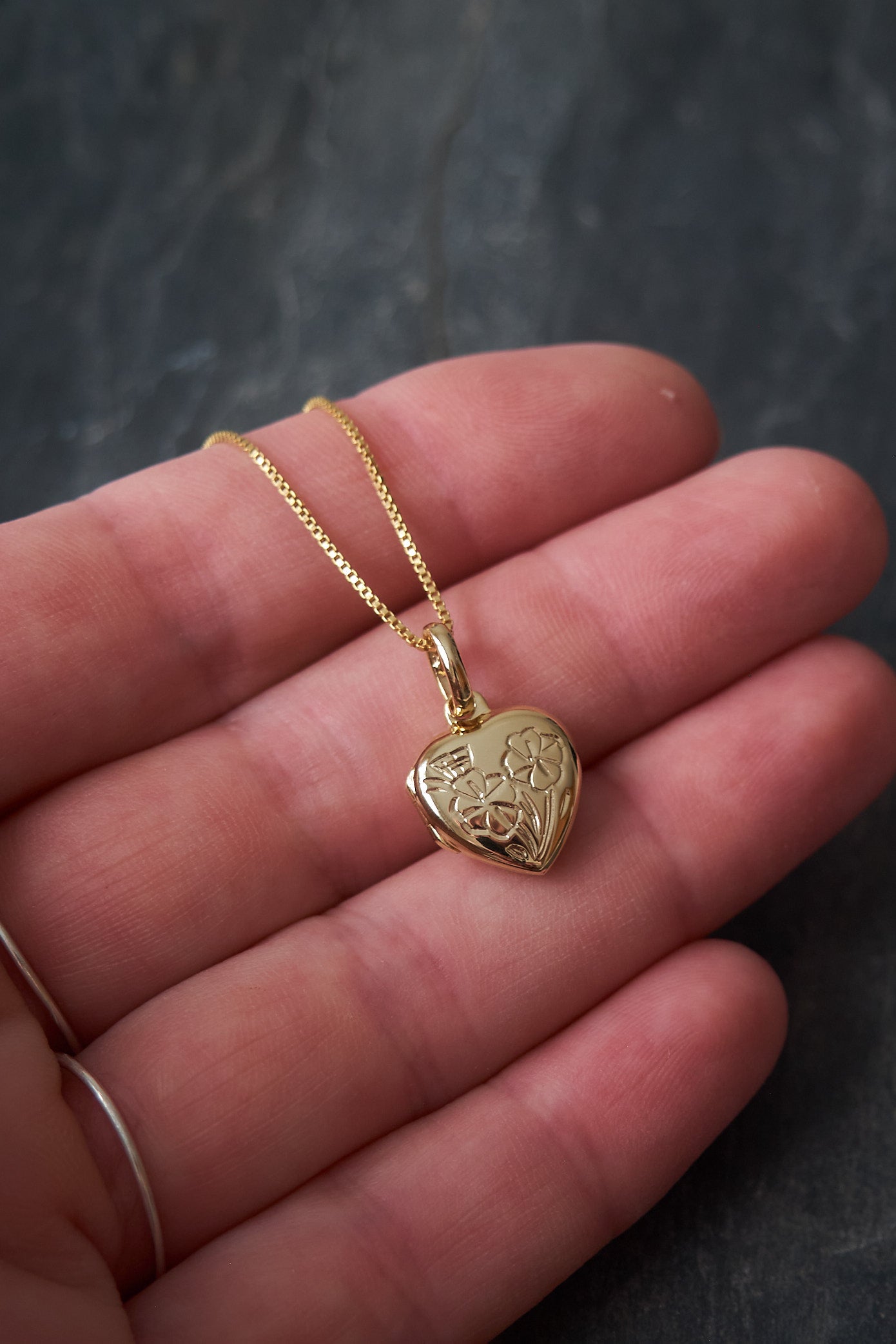 Gold heart-shaped locket on a chain held in a hand against a dark background