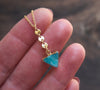 A gold edged, triangle gemstone necklaces with coin detail in hand