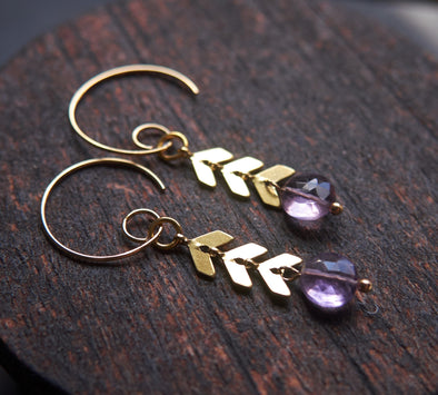 Modern amethyst earrings with gold chevron chain detail on a wooden background