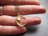 Matte gold crescent moon necklace with delicate white moonstone accent displayed in hand 