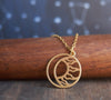 Round, matte gold moon and sun circle necklace resting on wood piece