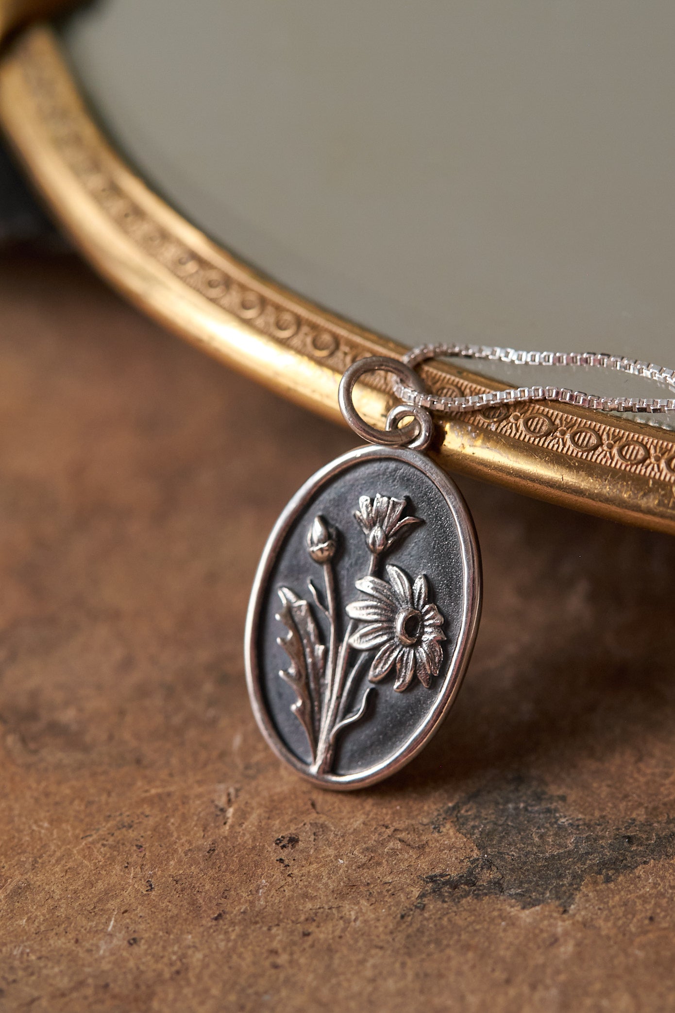 Close-up of a silver pendant with floral design on a textured surface