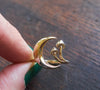 Gold crescent moon and mushroom ring held in fingers
