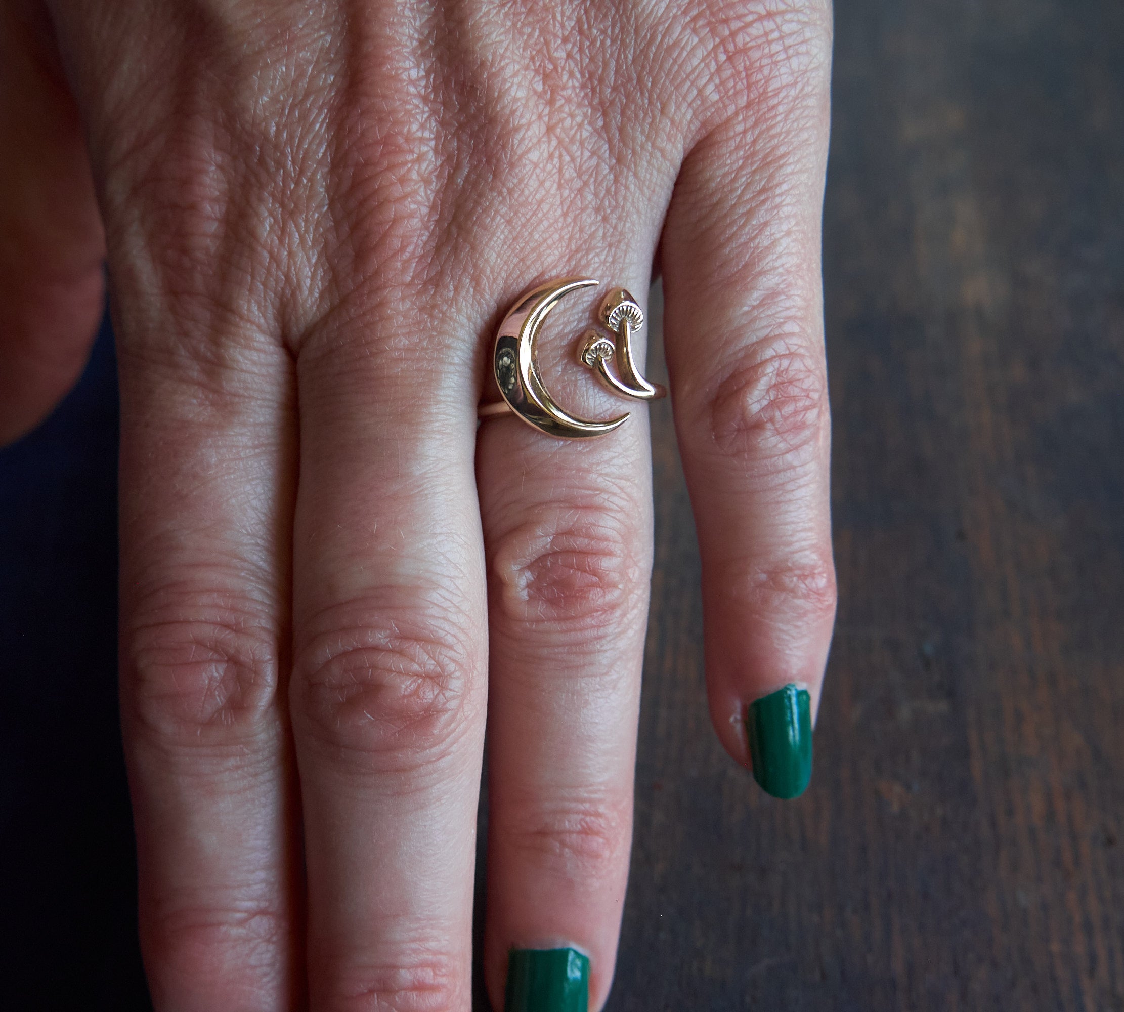 Close up of gold crescent moon and mushroom ring on hand