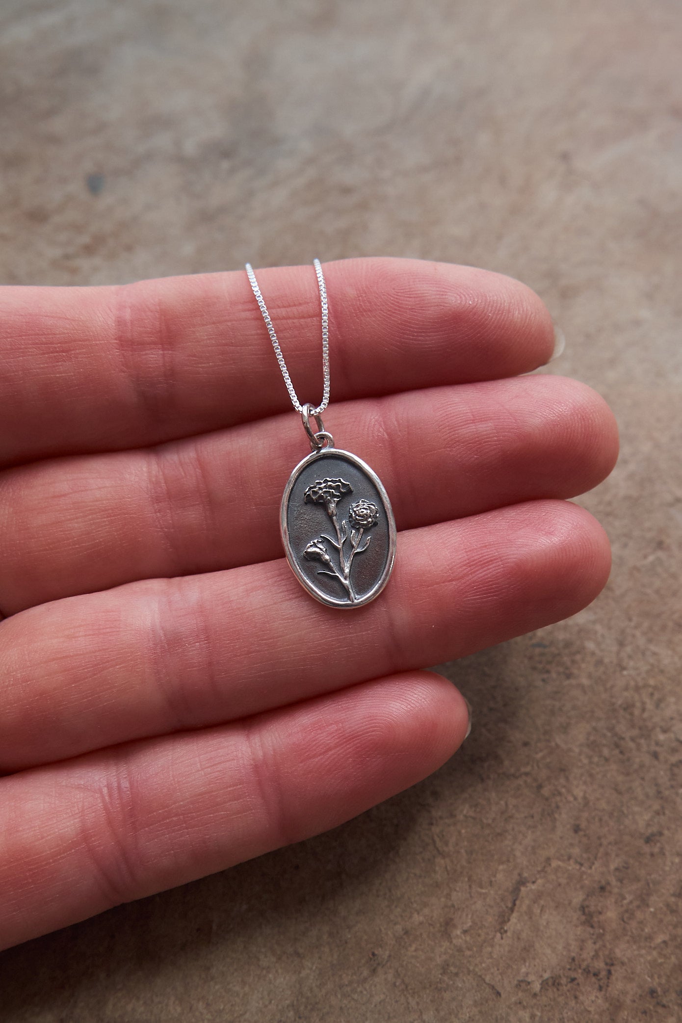 Silver January Birthflower necklace held in a hand on a neutral background