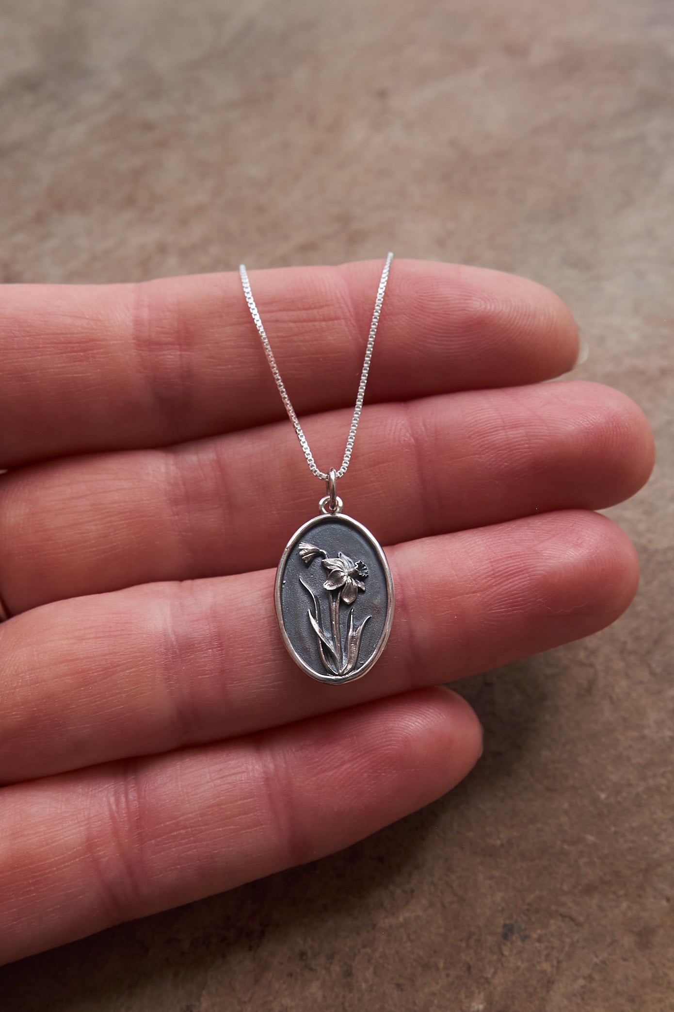 Silver necklace with a floral pendant on fingers on a brown slate background