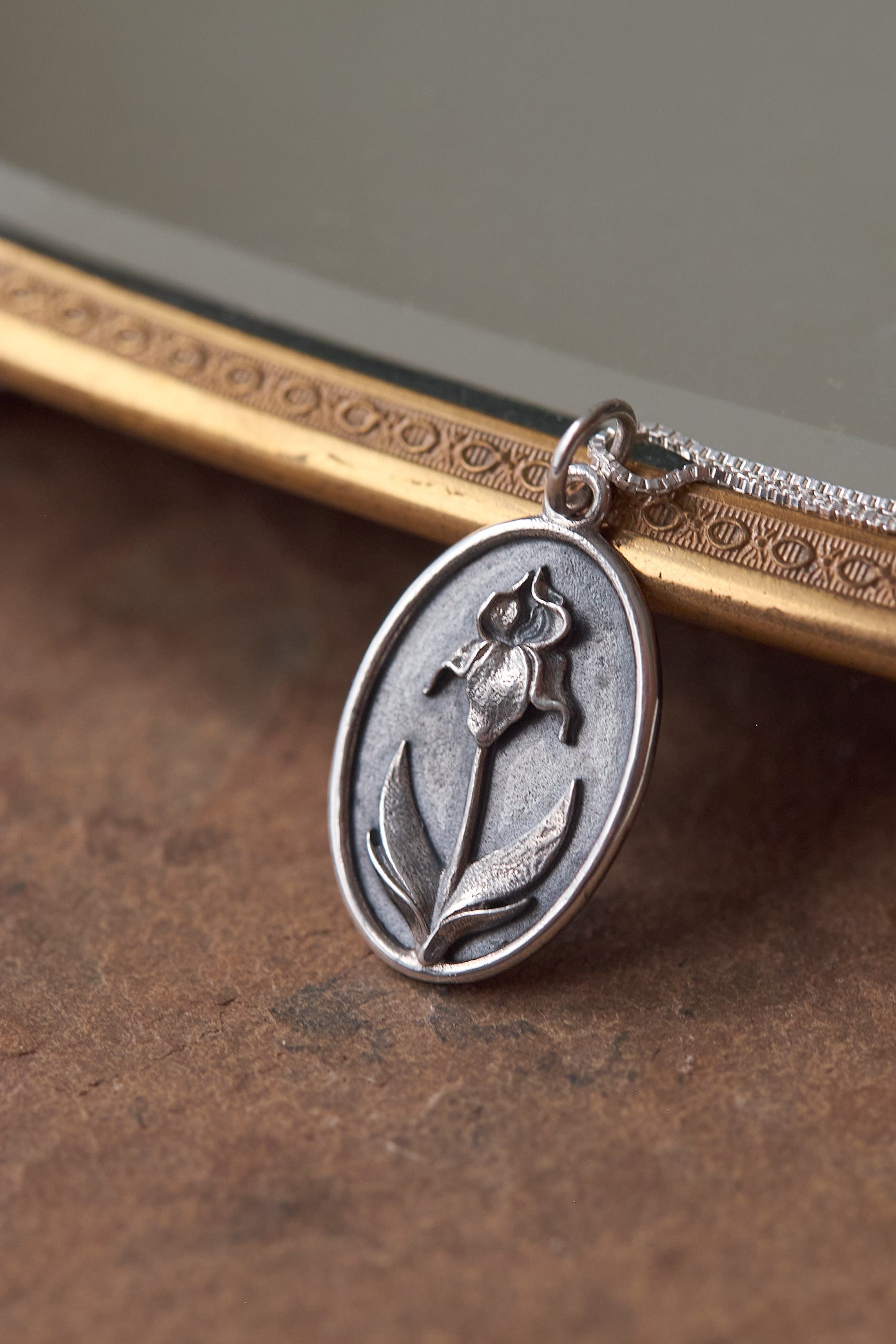Silver pendant with an iris flower design on a chain against a brown background