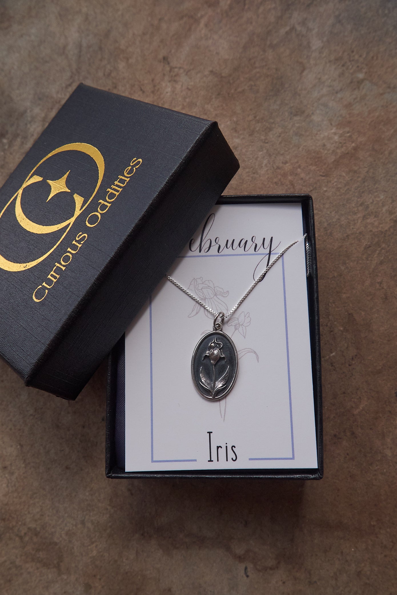 Silver necklace with flower pendant in a 'Curious Oddities' box on a textured surface