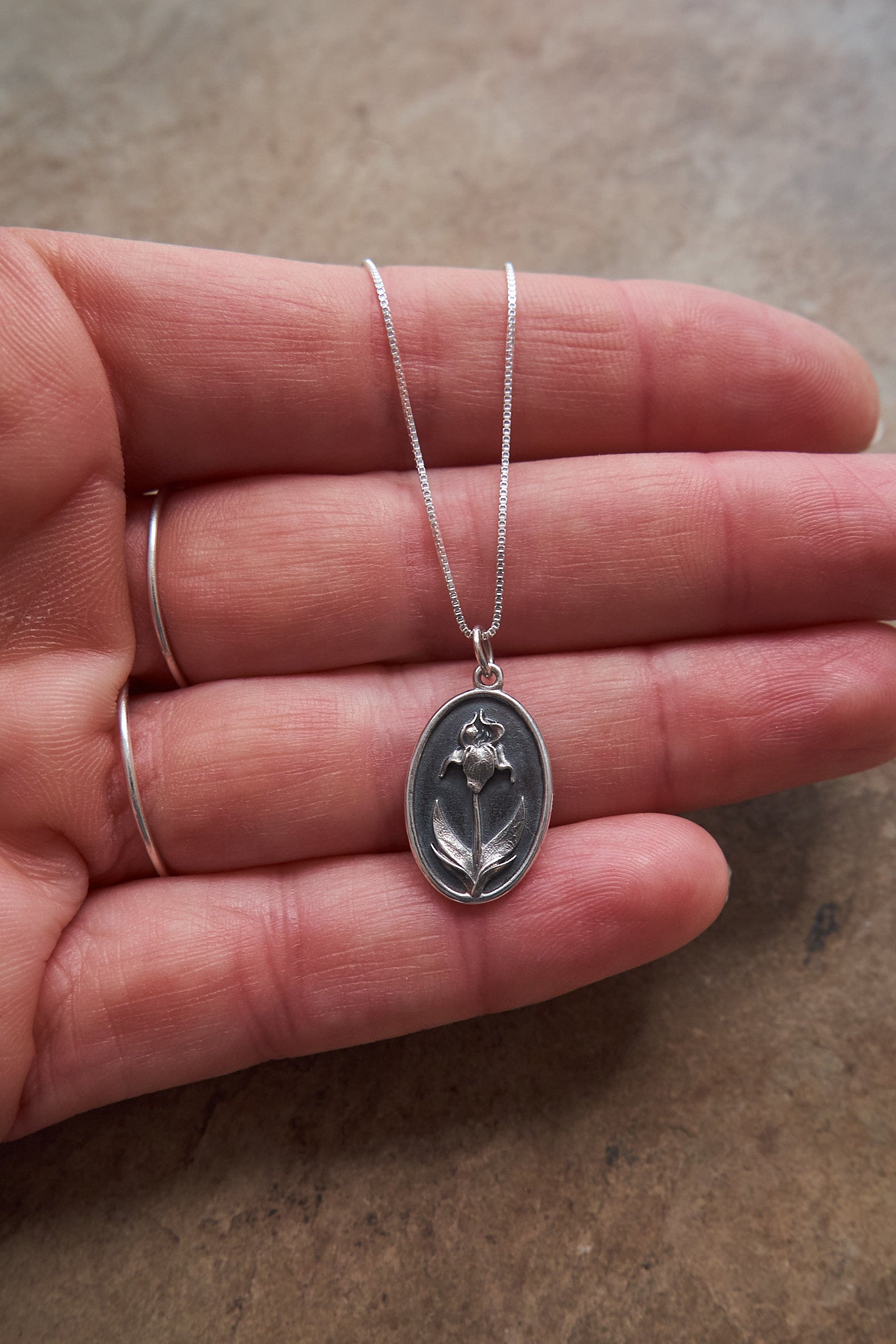 Silver necklace with an iris flower pendant held in a hand on a neutral background