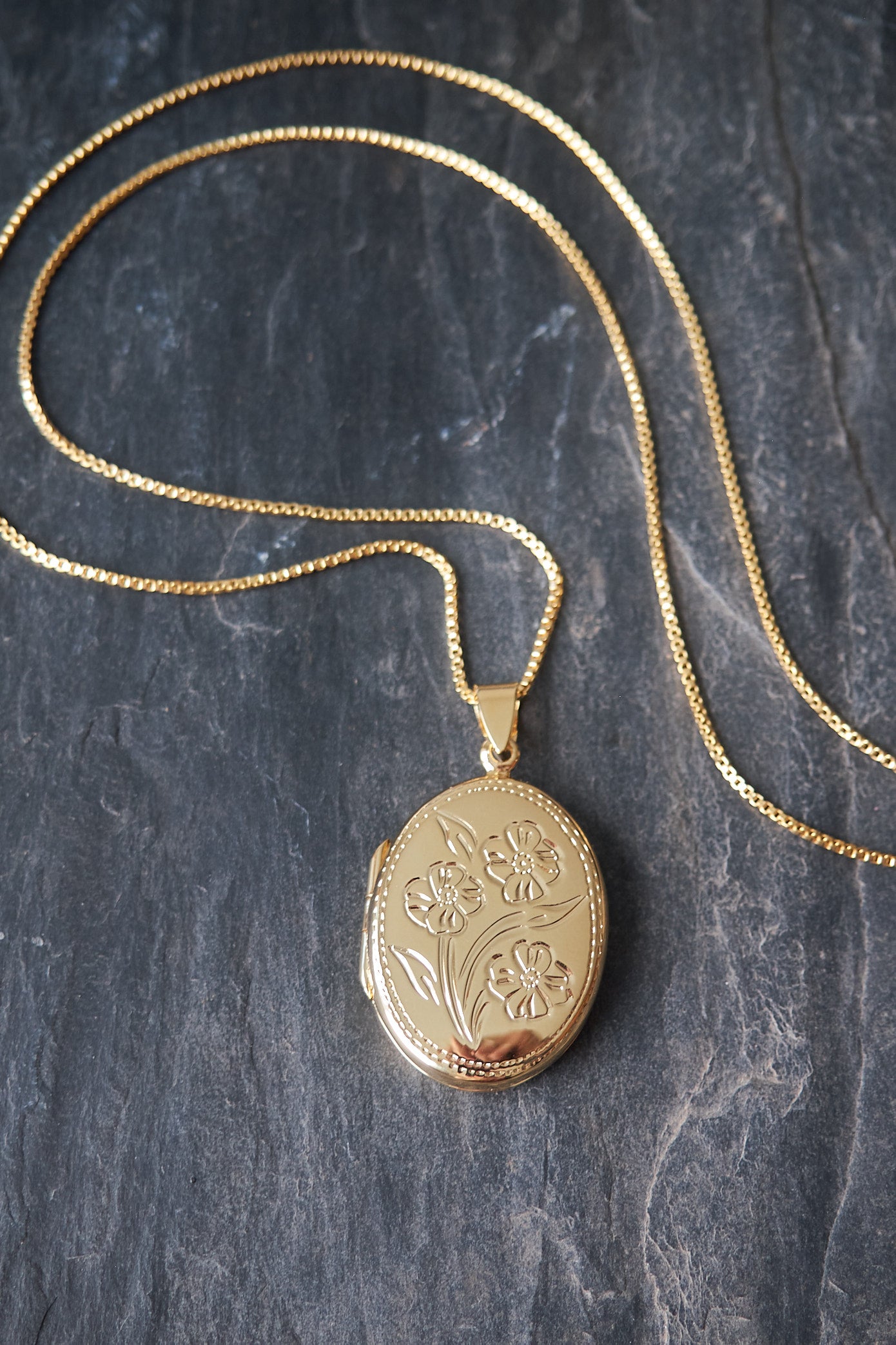 Gold oval locket necklace on a dark stone surface