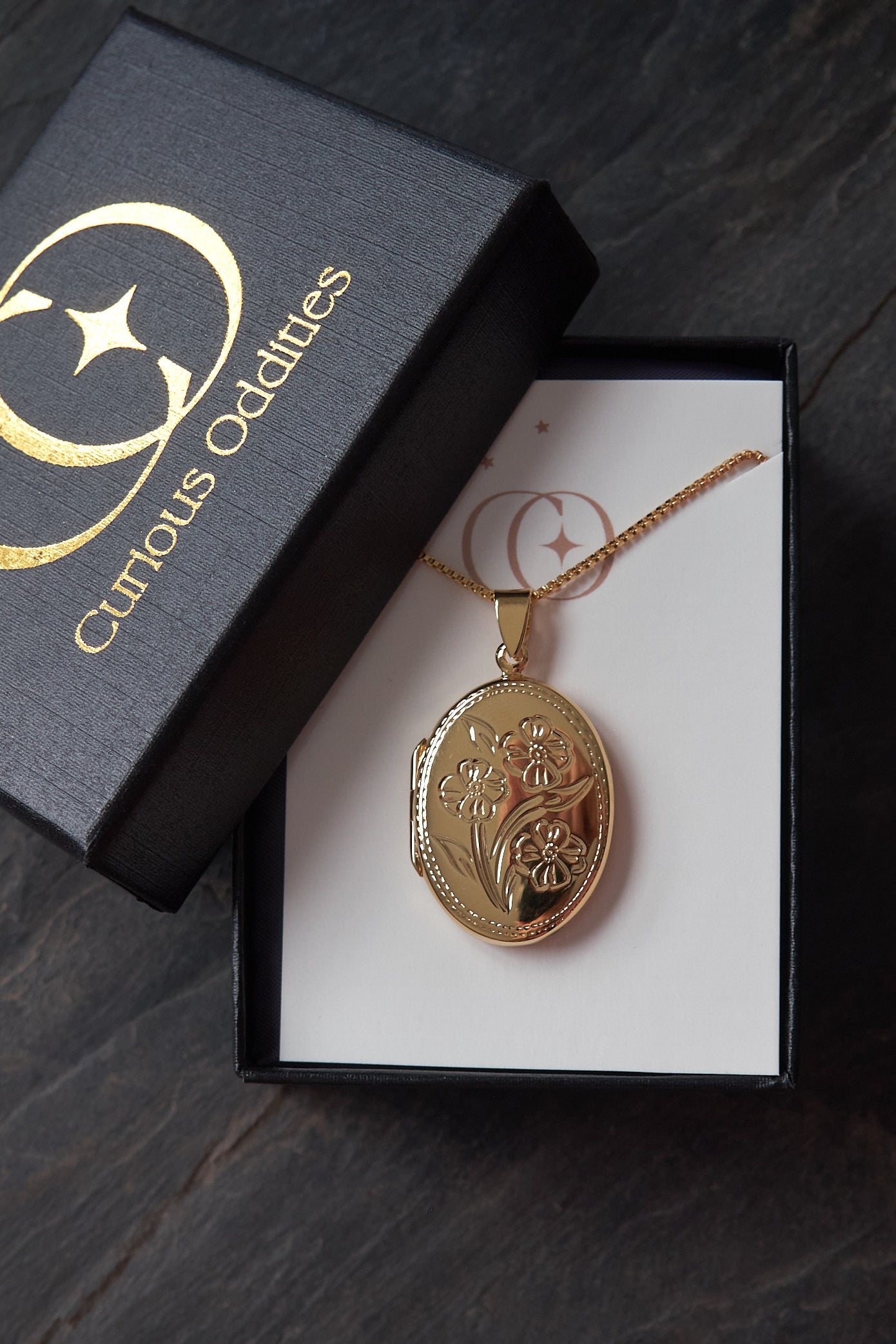 Gold locket necklace in a 'Curious Oddities' box on a dark surface