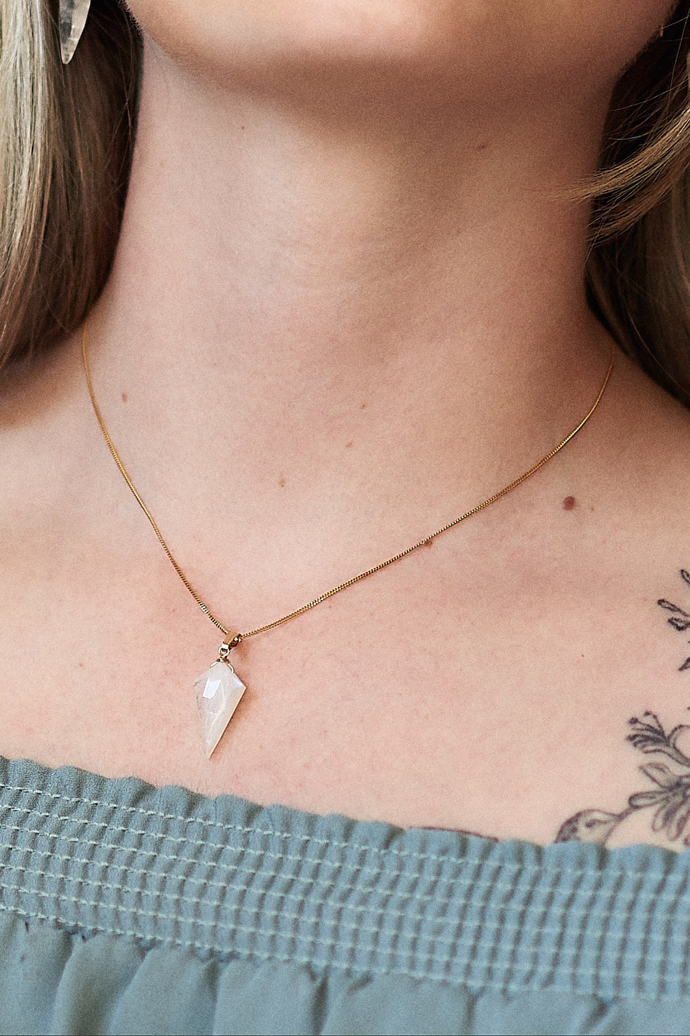 Necklace with a moonstone dagger shaped pendant worn by a person, focusing on the jewelry.