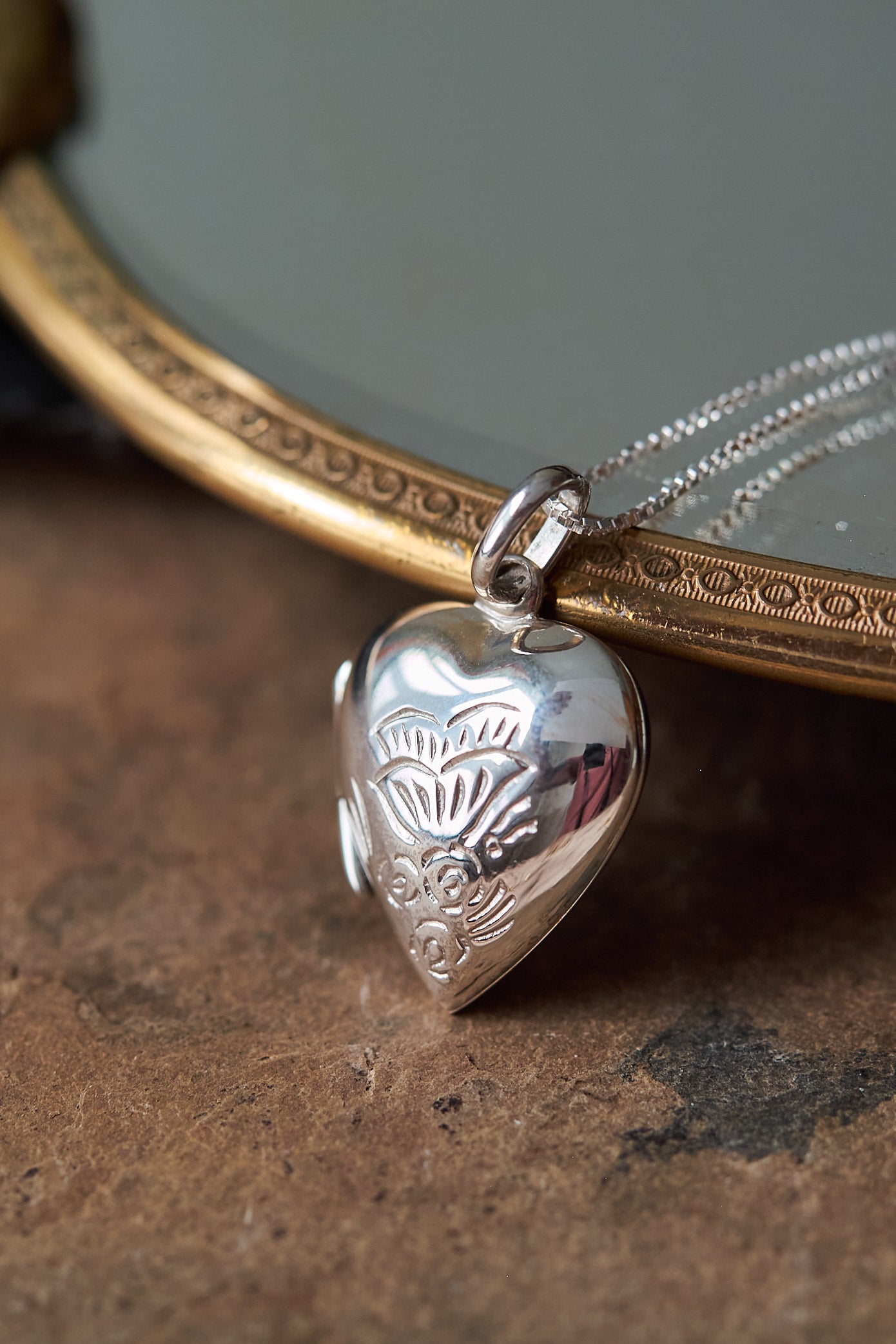 Silver heart-shaped locket on a chain against a textured surface