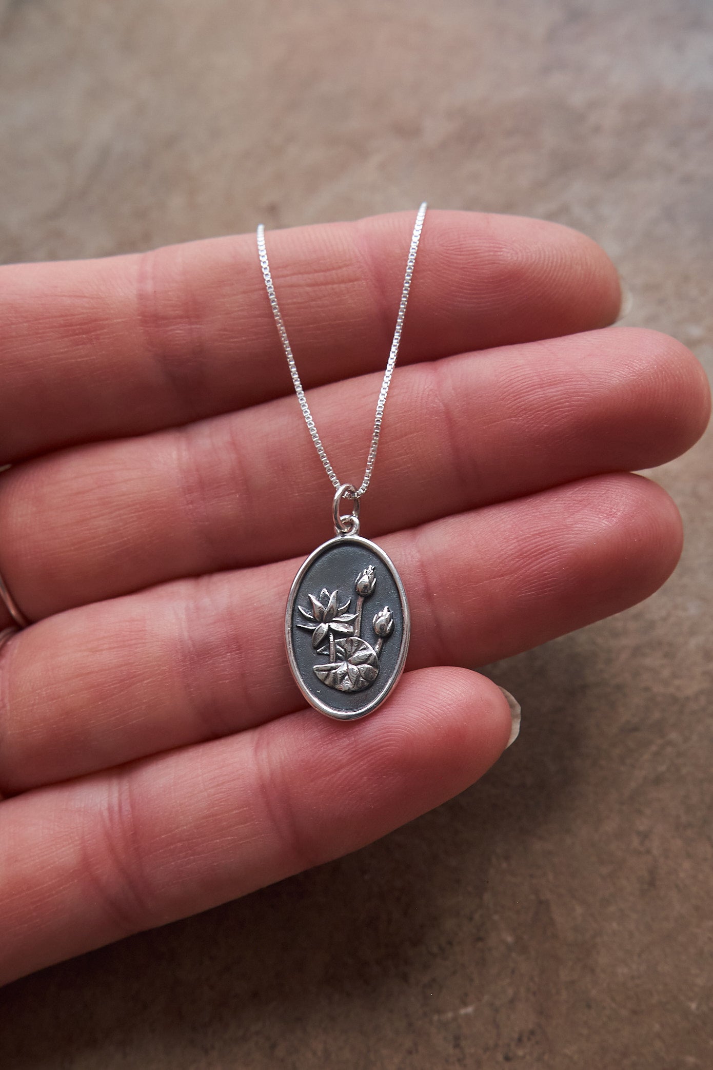 Silver necklace with a pendant held on hand on a brown slate surface