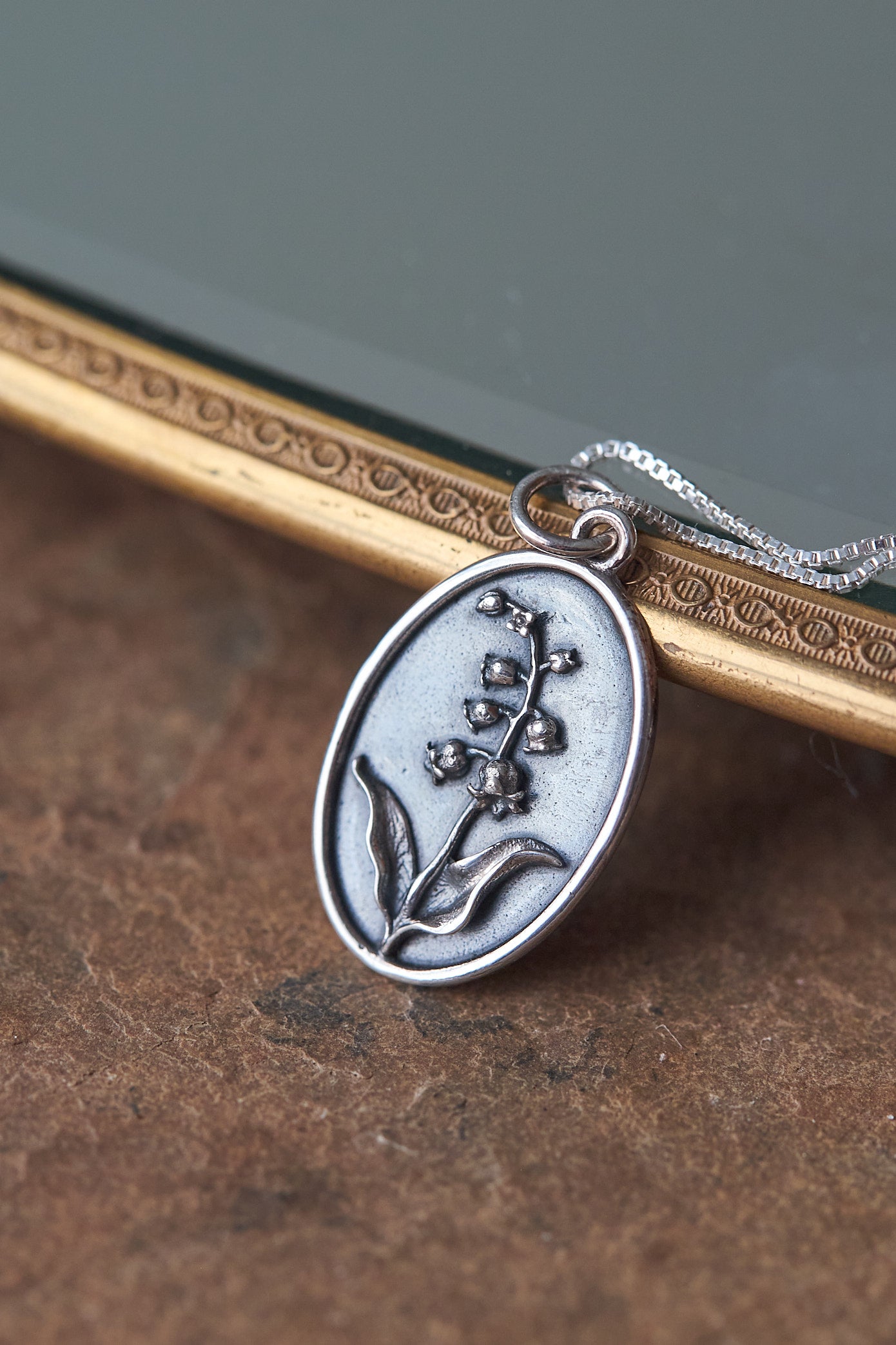 Silver necklace with a lily of the valley floral pendant on a textured surface