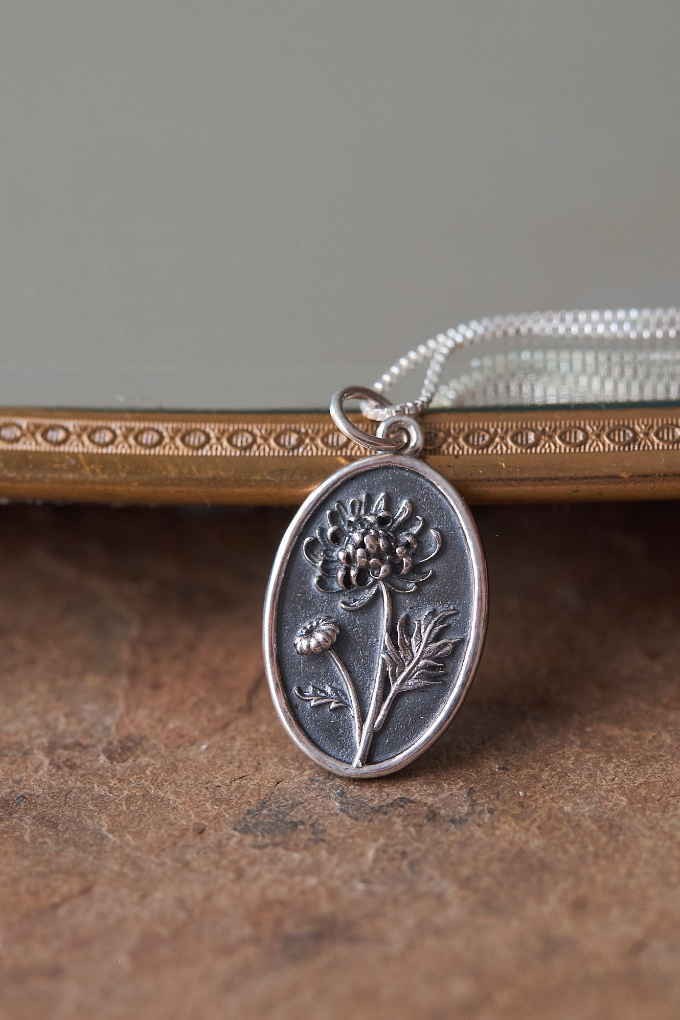 Silver pendant with chrysanthemum design on a textured surface