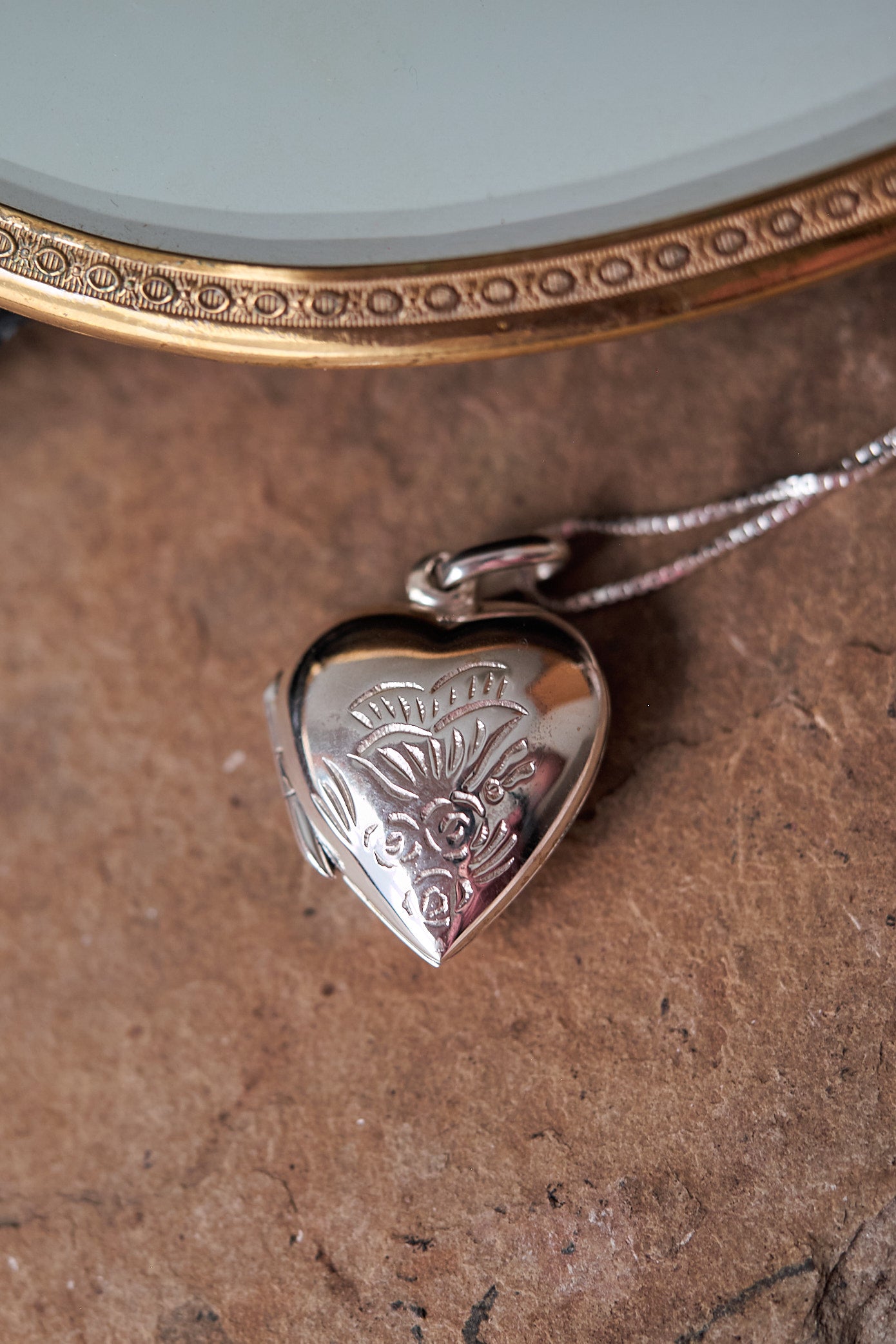 Heart-shaped silver locket with floral engraving on a brown surface