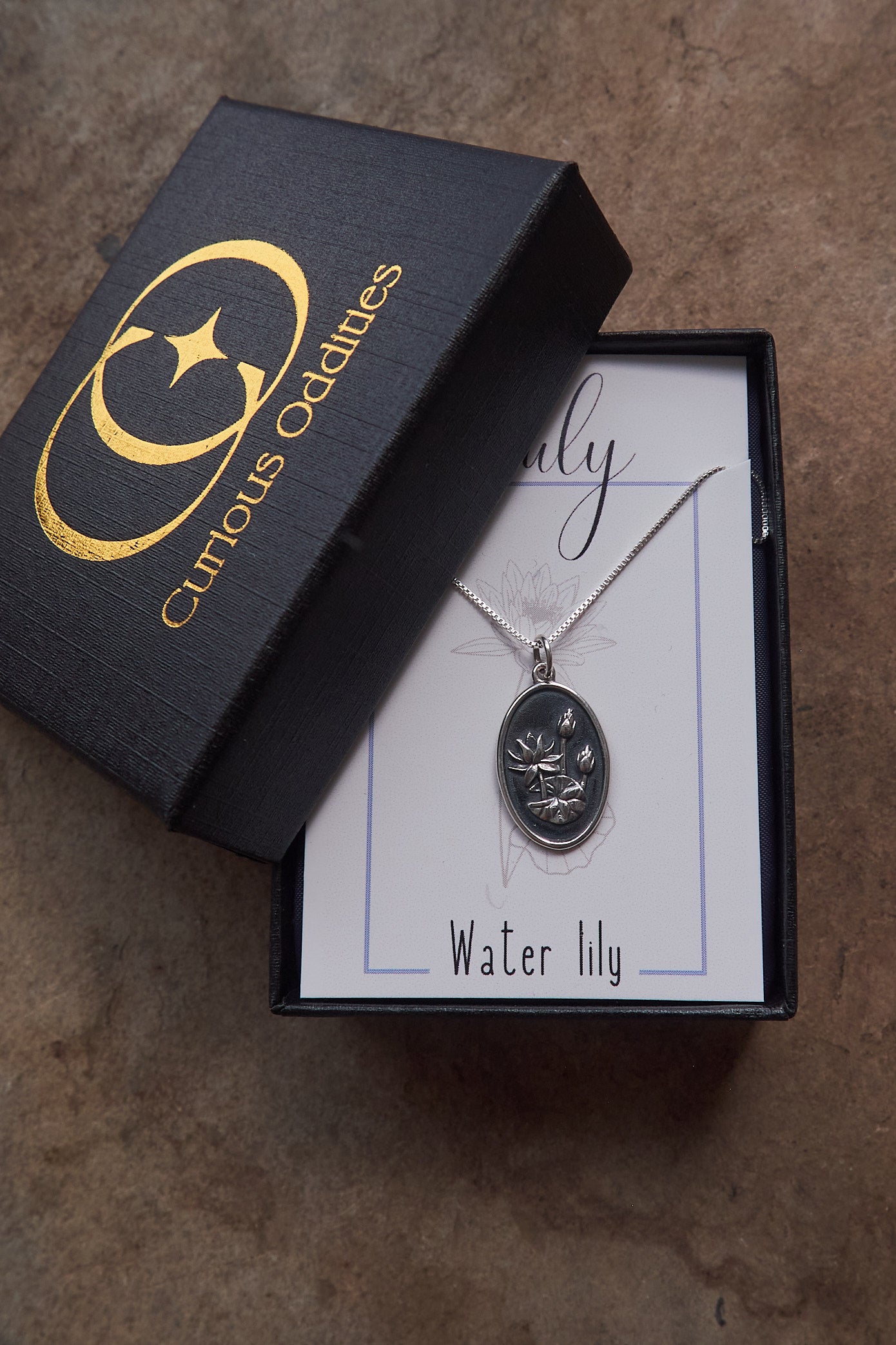Silver necklace with waterlily pendant in a 'Curious Oddities' box on a textured surface
