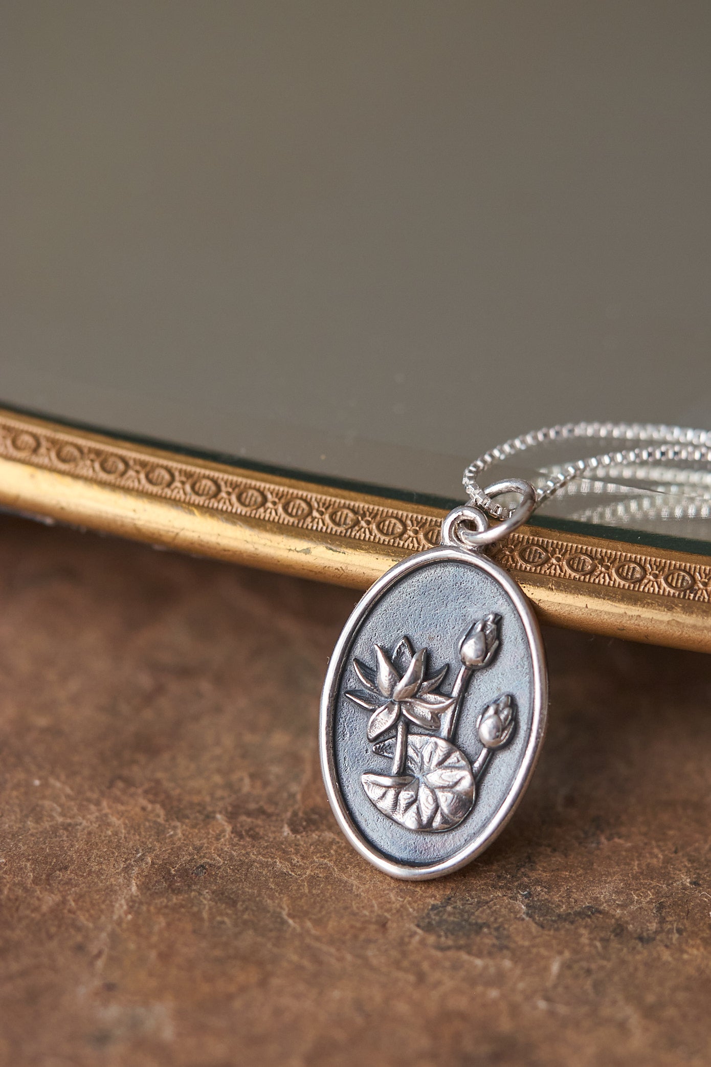 Silver pendant with waterlily design on a brown slate surface